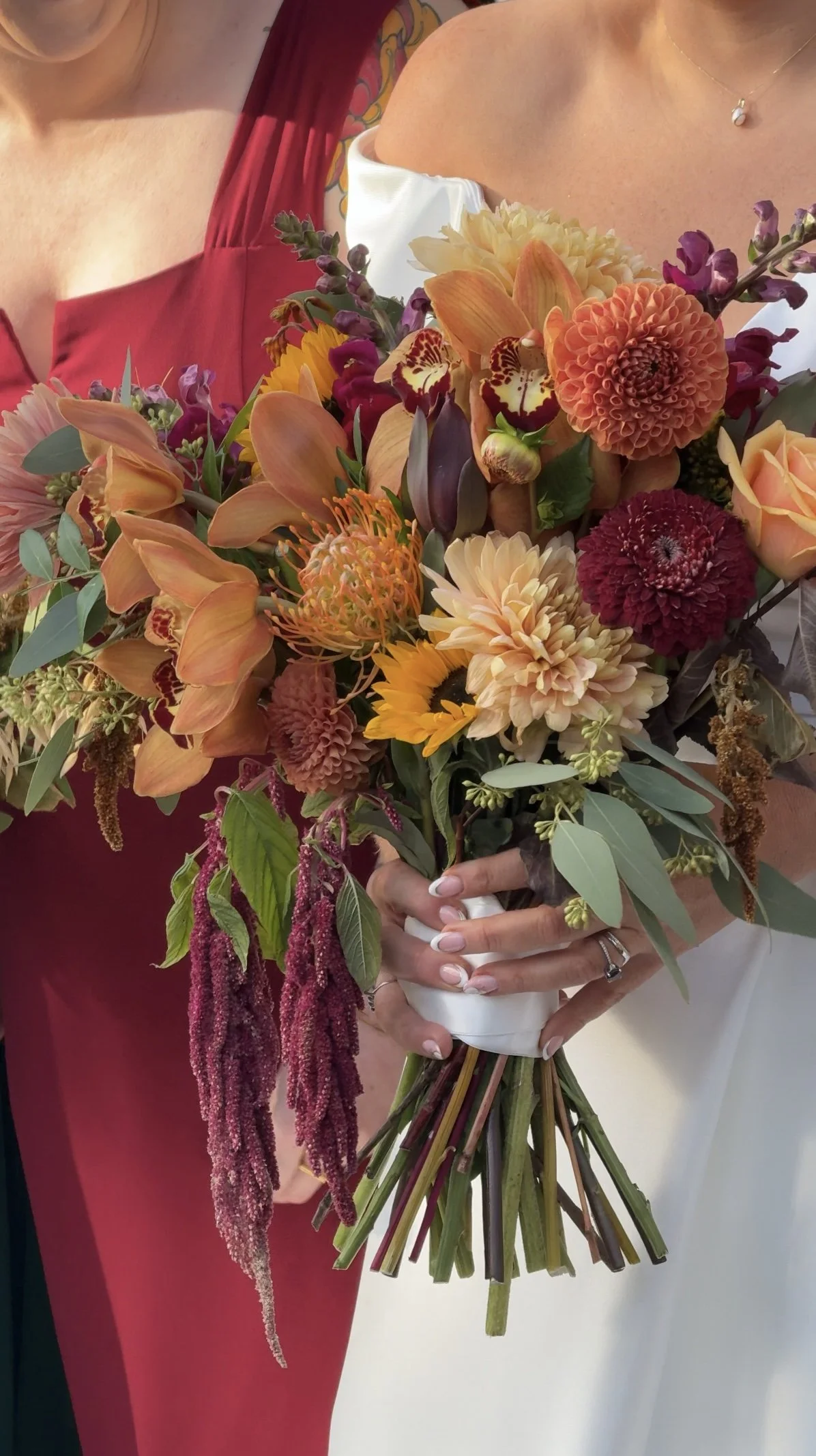 Close-up of a woman holding a large, colorful bouquet of fall flowers, including orange, yellow, and burgundy blooms, with a white ribbon around the stems.
