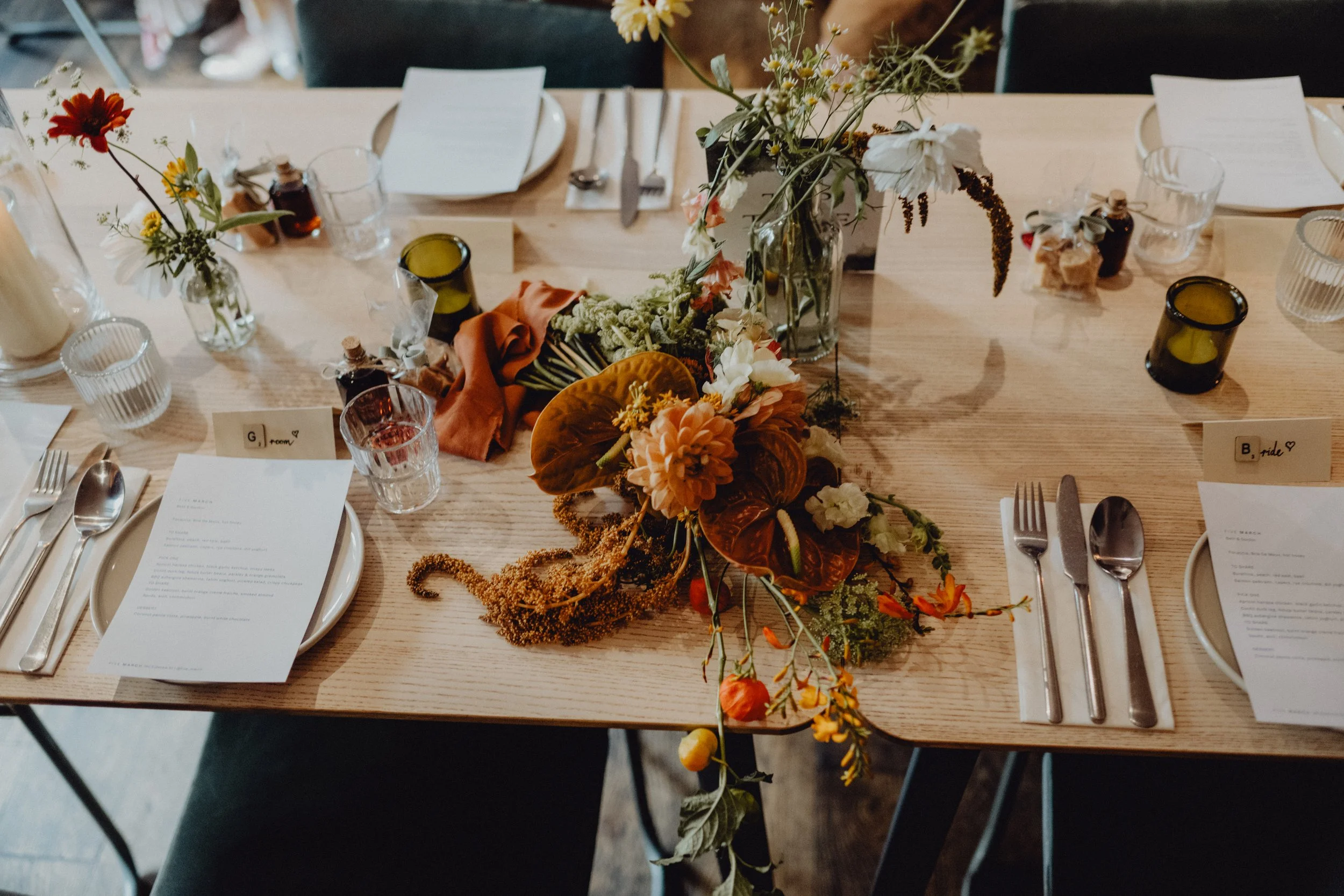A decorated table set for a wedding or special event with a floral centerpiece, candles, and place settings including menus and directional cards.