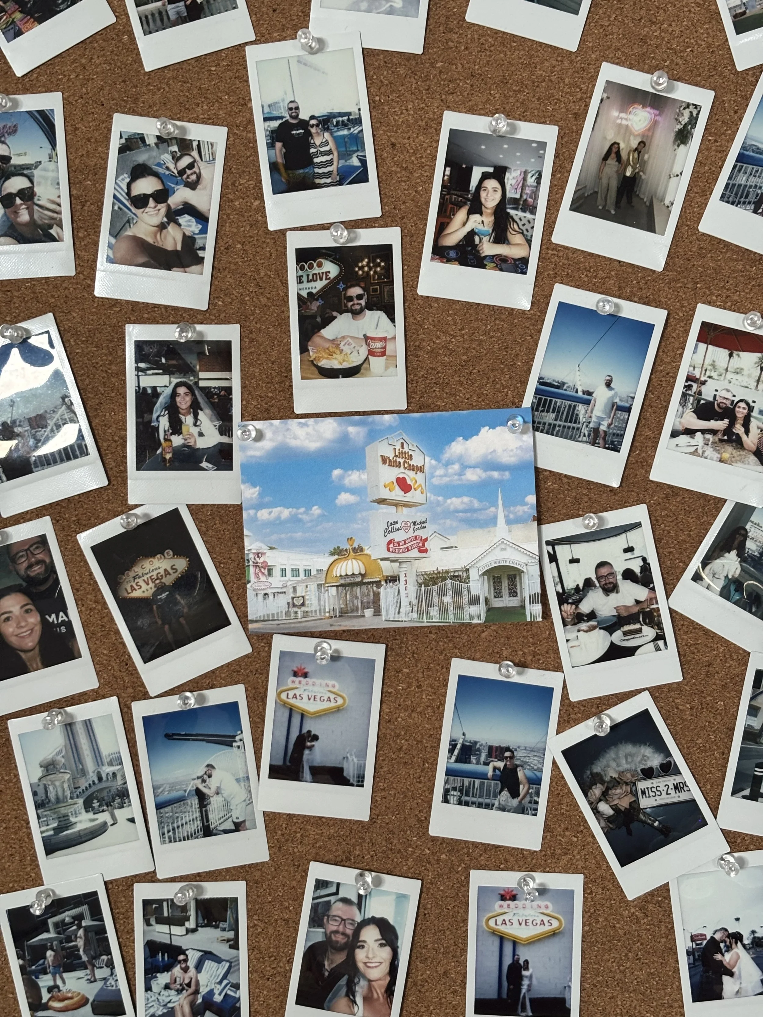 A corkboard covered with various Polaroid photos of people, places, and objects, with a central photo of the "Little White Chapel" sign in Las Vegas. The photos depict individuals, couples, and scenic views, primarily taken outdoors and indoors, celebrating occasions, and enjoying leisure activities.