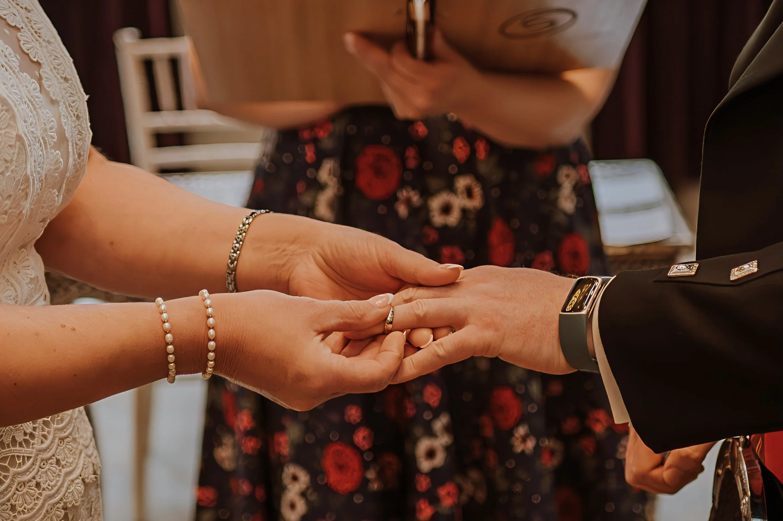 Close-up of a wedding ceremony with a bride and groom exchanging rings, with an officiant in the background.