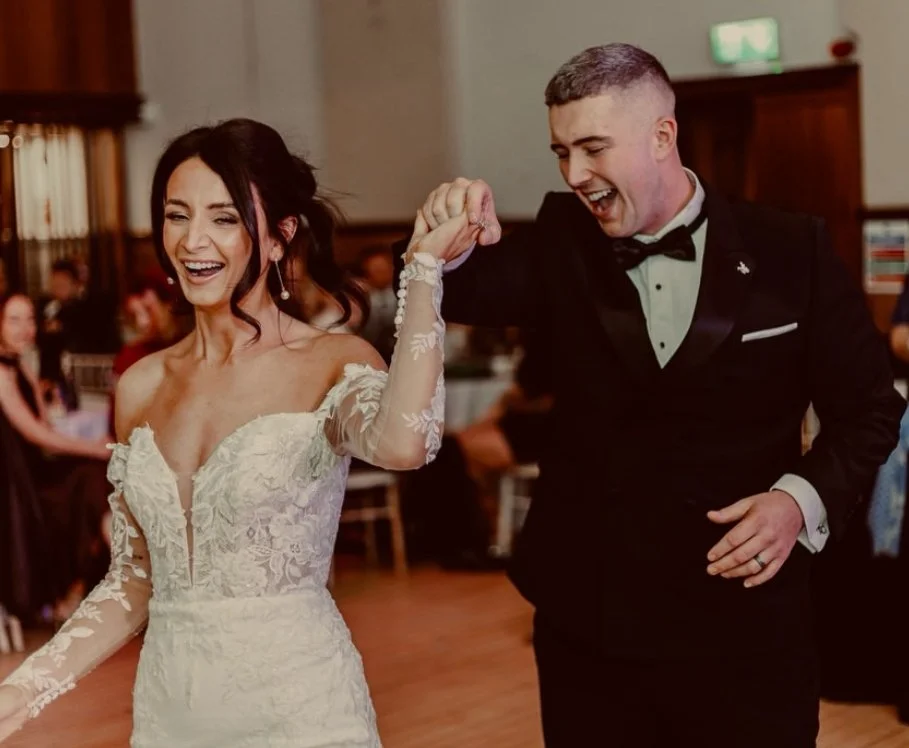 A bride and groom dancing and smiling at their wedding reception, holding hands in the air.