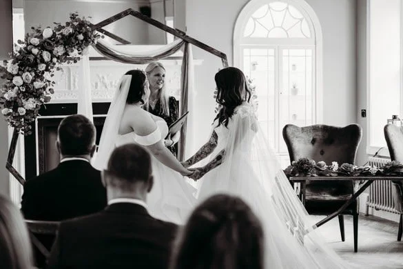 Bride and partner holding hands during wedding ceremony with officiant in a decorated indoor setting.