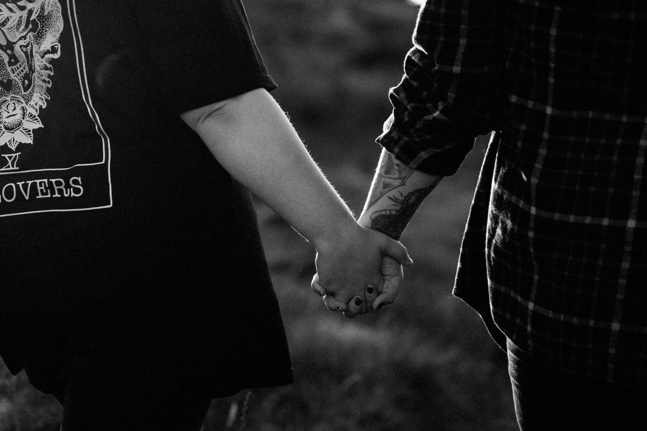 A close-up black and white photo of two people holding hands, one wearing a short-sleeved shirt and the other wearing a long-sleeved plaid shirt.