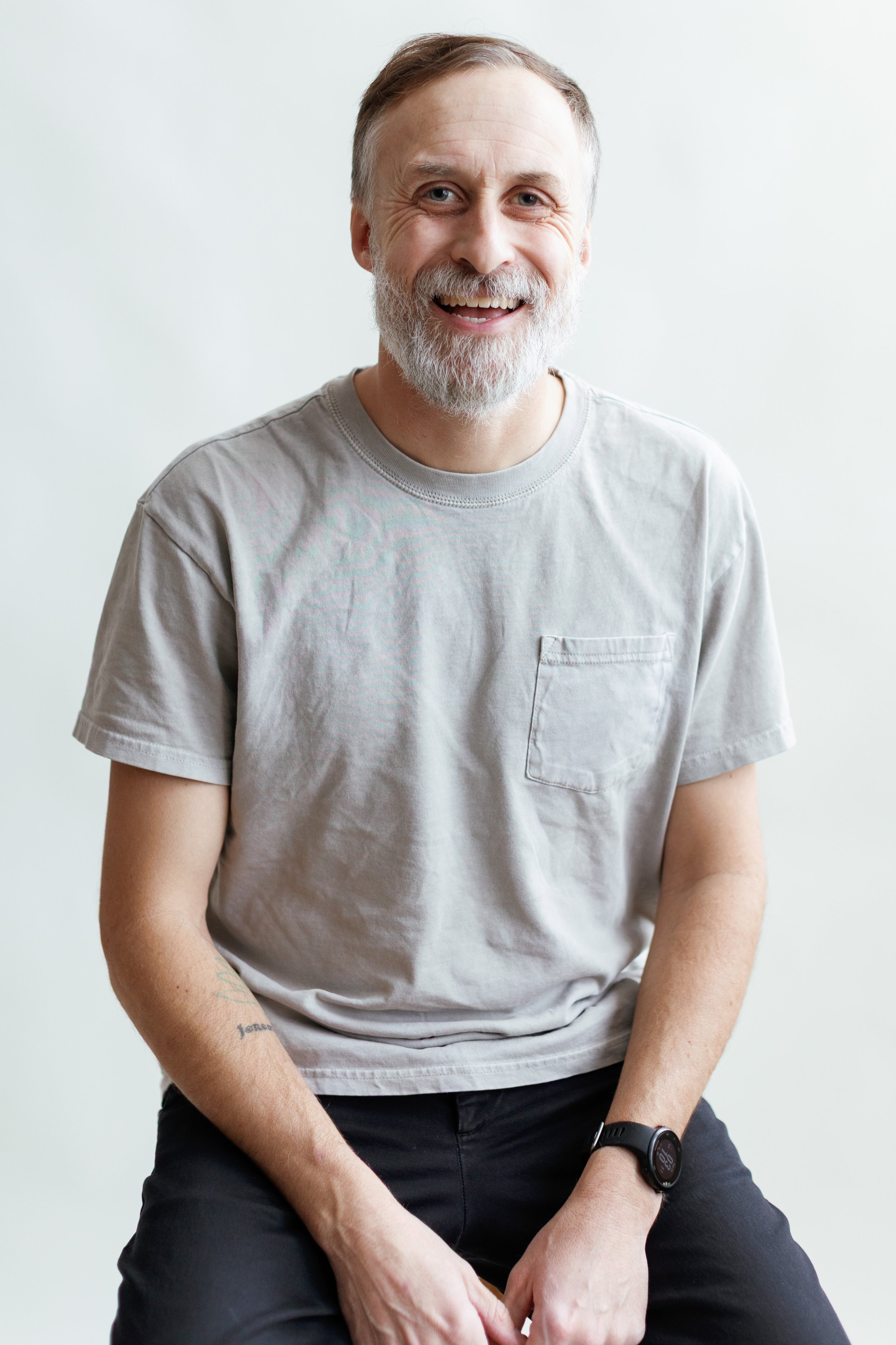 Black and white portrait of a smiling middle-aged man with shoulder-length wavy hair and a beard, wearing a collared shirt.