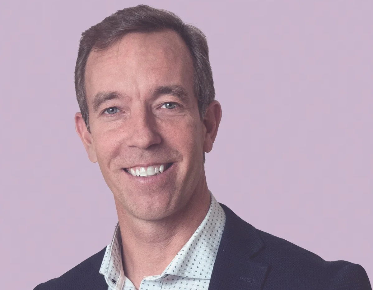 Portrait of a smiling man in a business suit with a light purple background.
