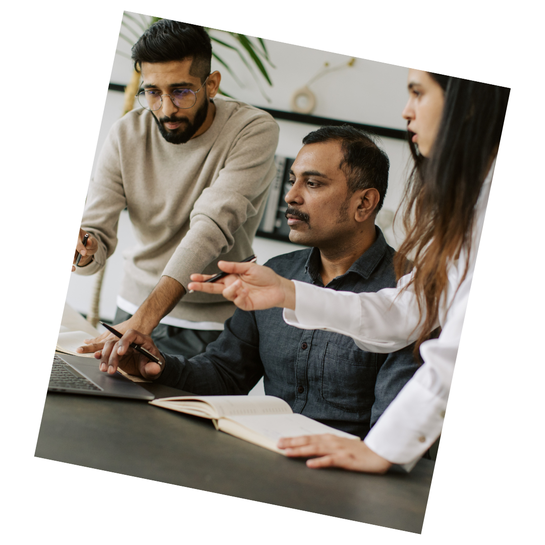 Three colleagues discussing around a laptop and notebooks in a modern office.