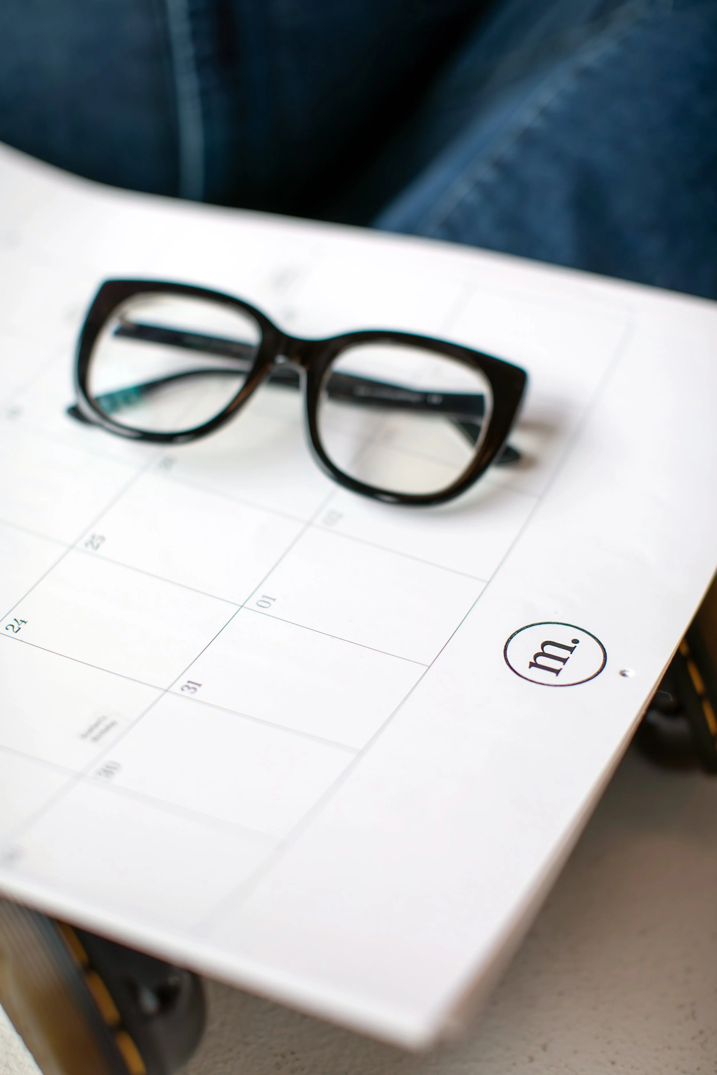 Black eyeglasses resting on a white calendar page.