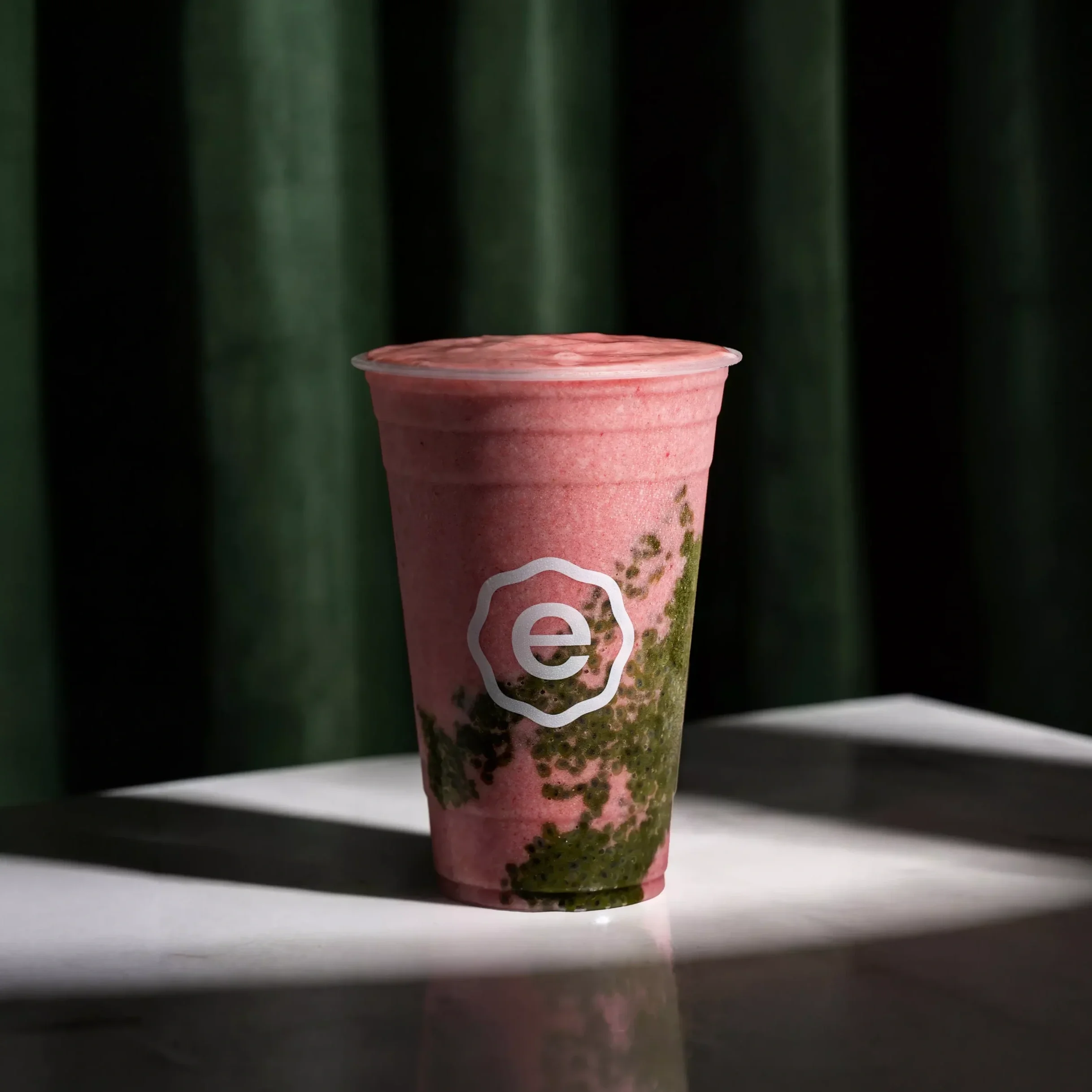A pink smoothie in a cup with a green and black background.