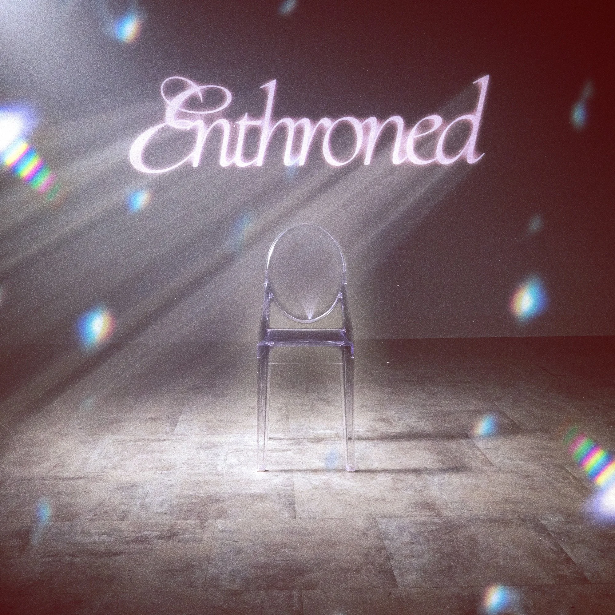 A clear chair in front of a wall with the word "Entranced" glowing in cursive. Light reflections are visible on the floor and wall.