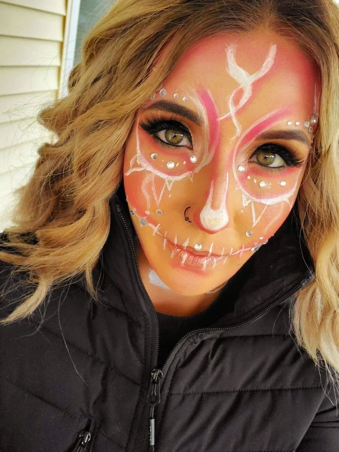 A woman with face paint resembling a sugar skull, decorated with colorful details and rhinestones, wearing a black jacket.