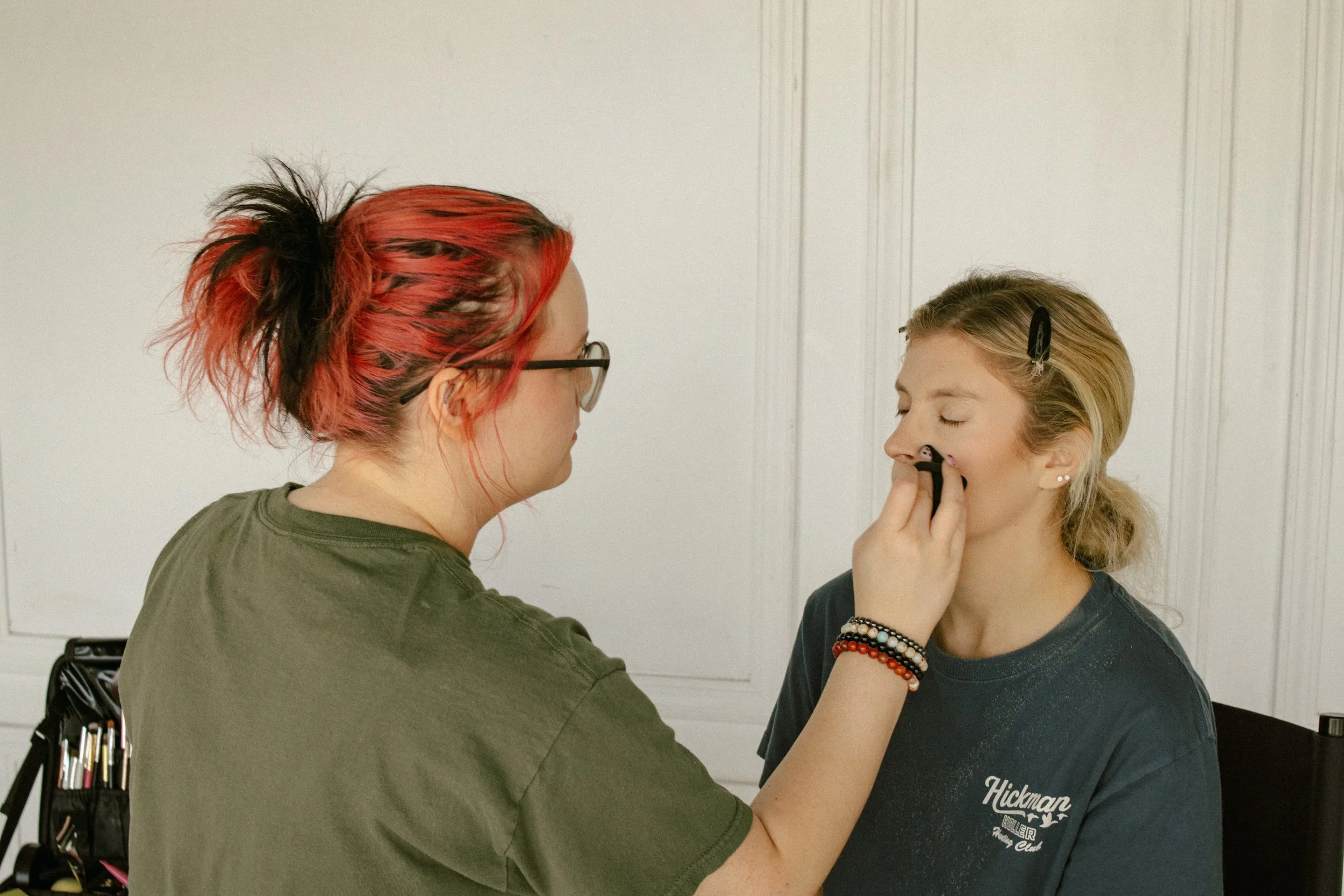 Makeup artist applying makeup to woman's face in a studio setting.