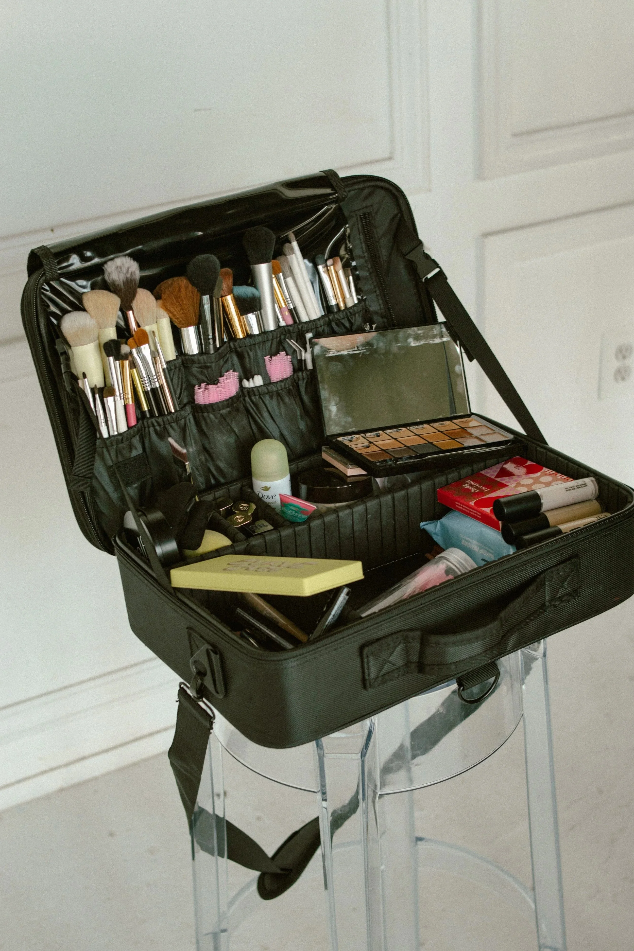 Open black makeup bag with organized brushes, makeup palette, and various cosmetics inside, placed on a clear acrylic makeup stand.