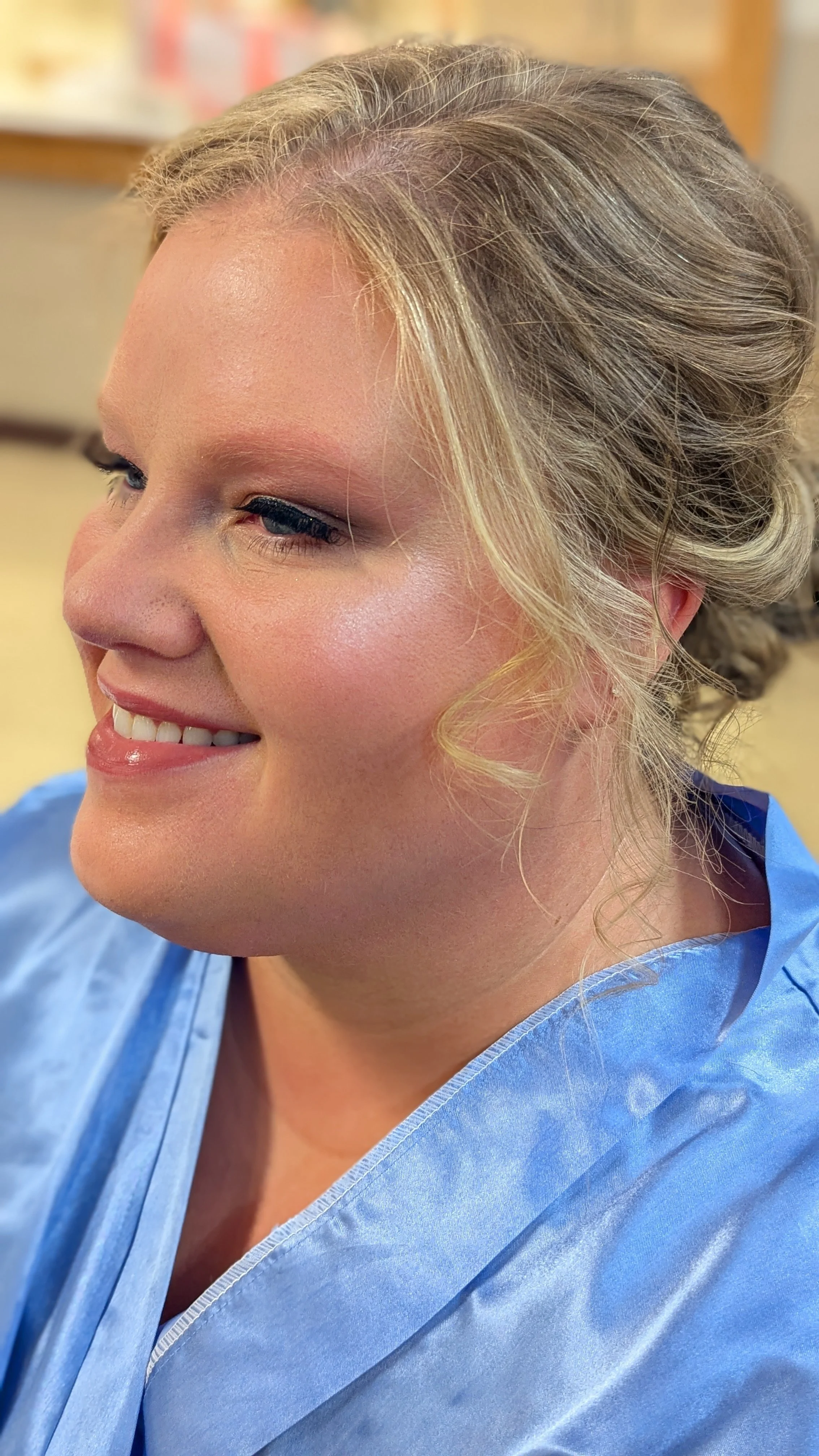 Close-up of a woman with blonde hair styled in an elegant updo, wearing blue medical scrubs.