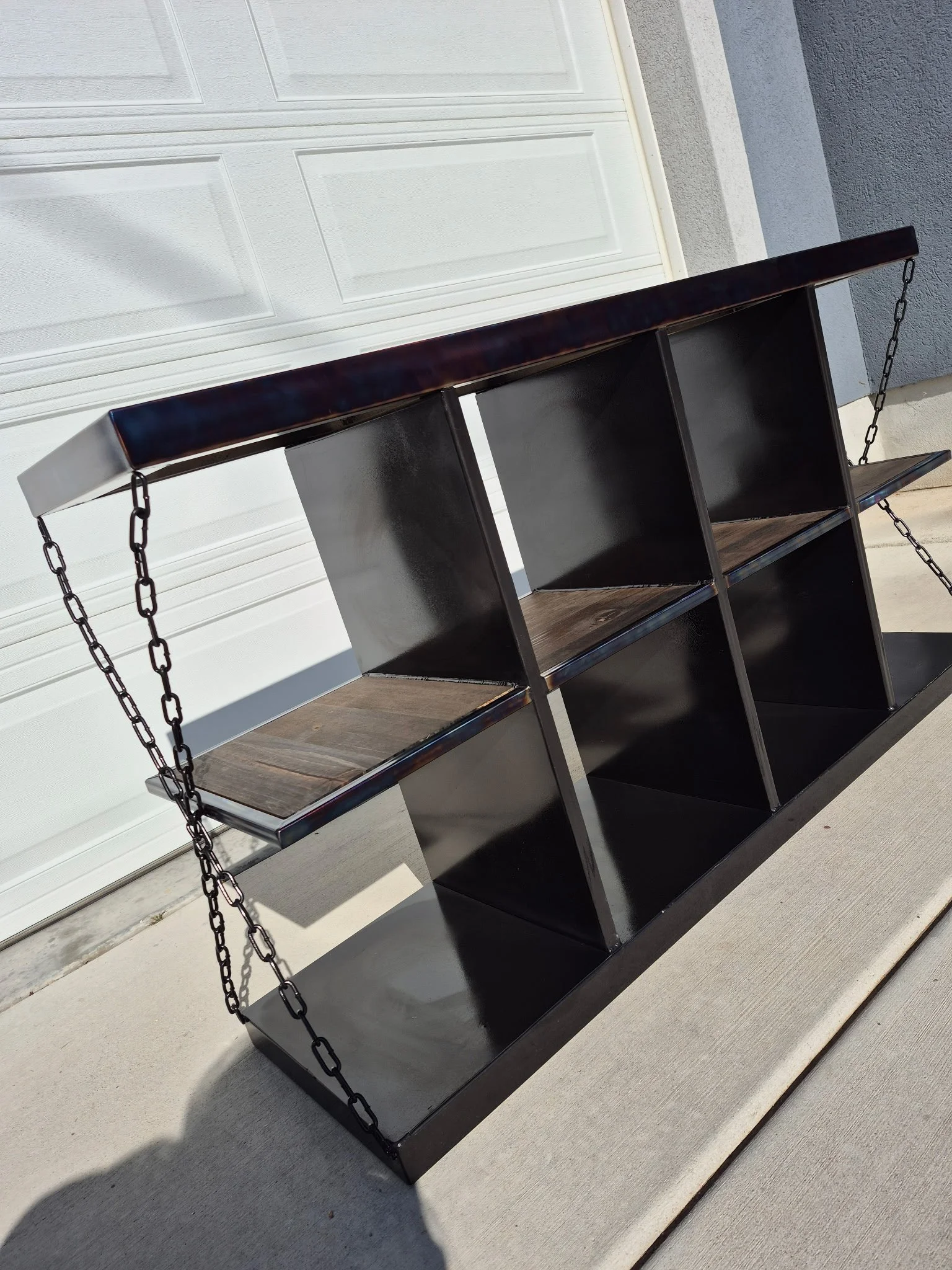 Industrial-style custom metal storage bench featuring a sleek black steel frame with a heat-treated patina finish, paired with a rich wood top and reinforced shelving. Unique chain side accents add a bold, rugged aesthetic, making this piece perfect 