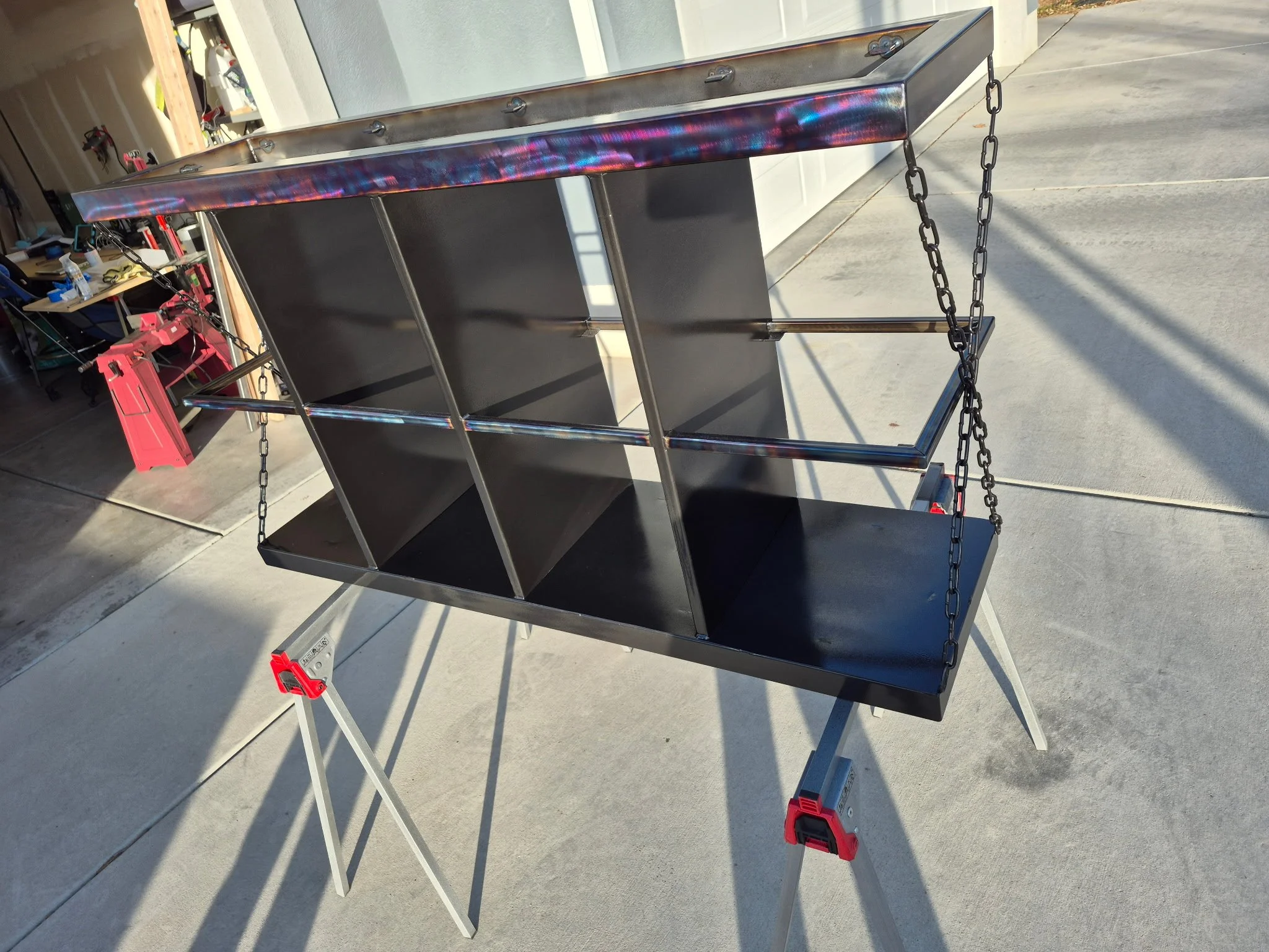 Industrial-style custom metal storage bench featuring a sleek black steel frame with a heat-treated patina finish. Unique chain side accents add a bold, rugged aesthetic, making this piece perfect for entryways, garages, mudrooms, or modern industria