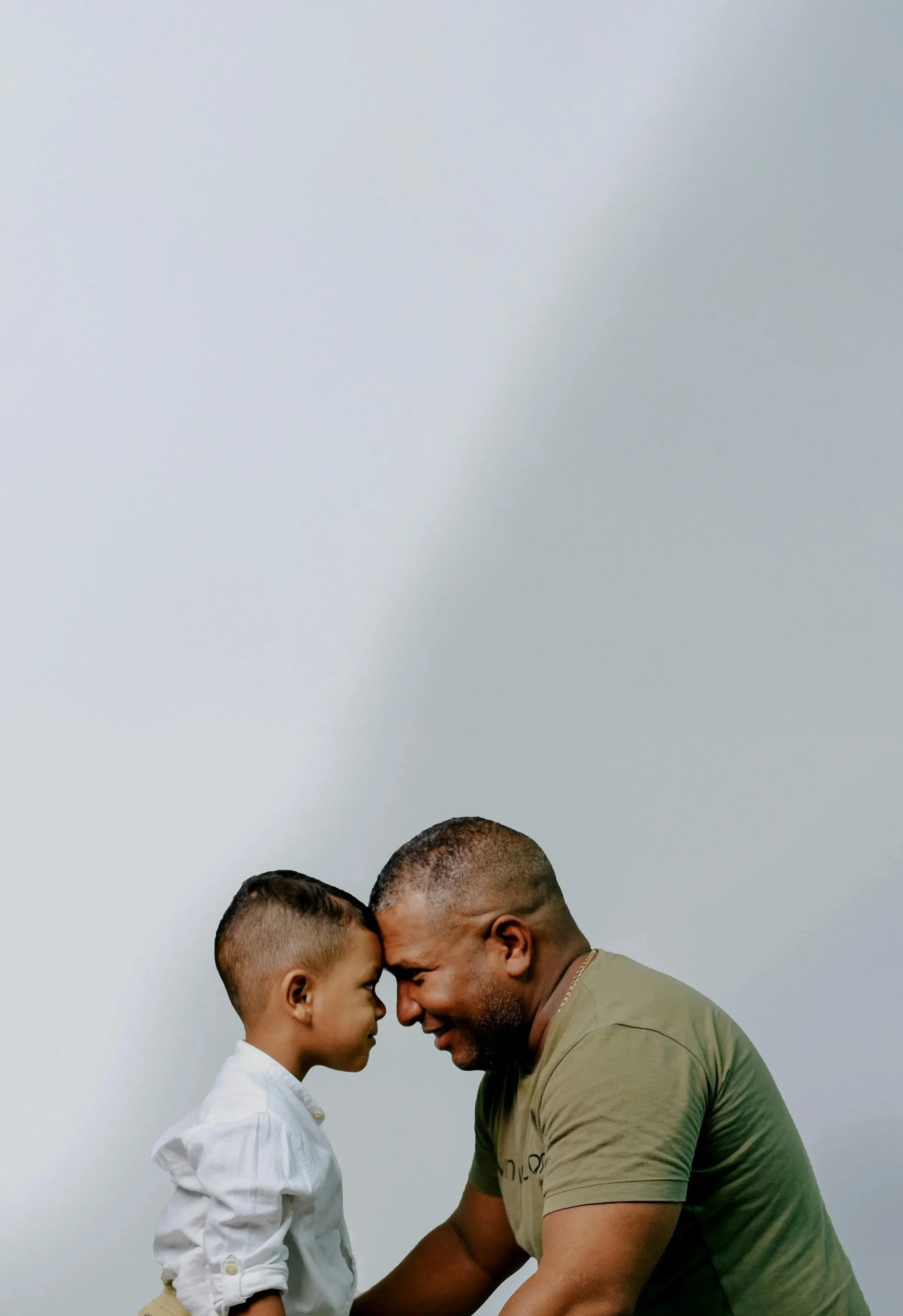 Adult man and young child lean their foreheads together while smiling softly, sharing calm and emotionally connected moment. Image reflects presence and trust often explored in internal family systems and ifs coaching for men.
