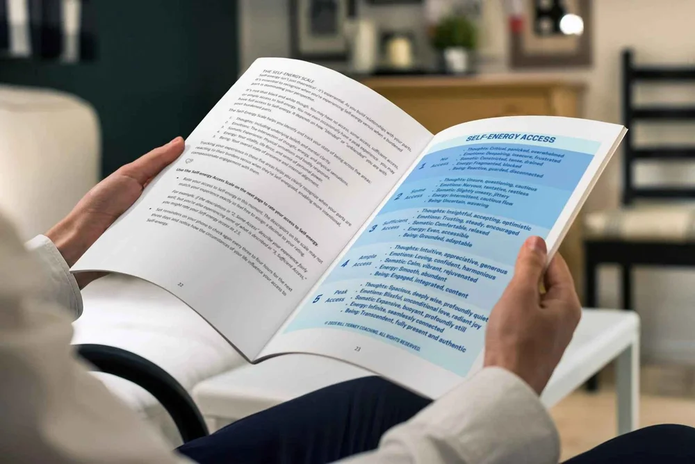 A person holding an open book with text about self-energy access in a living room setting.