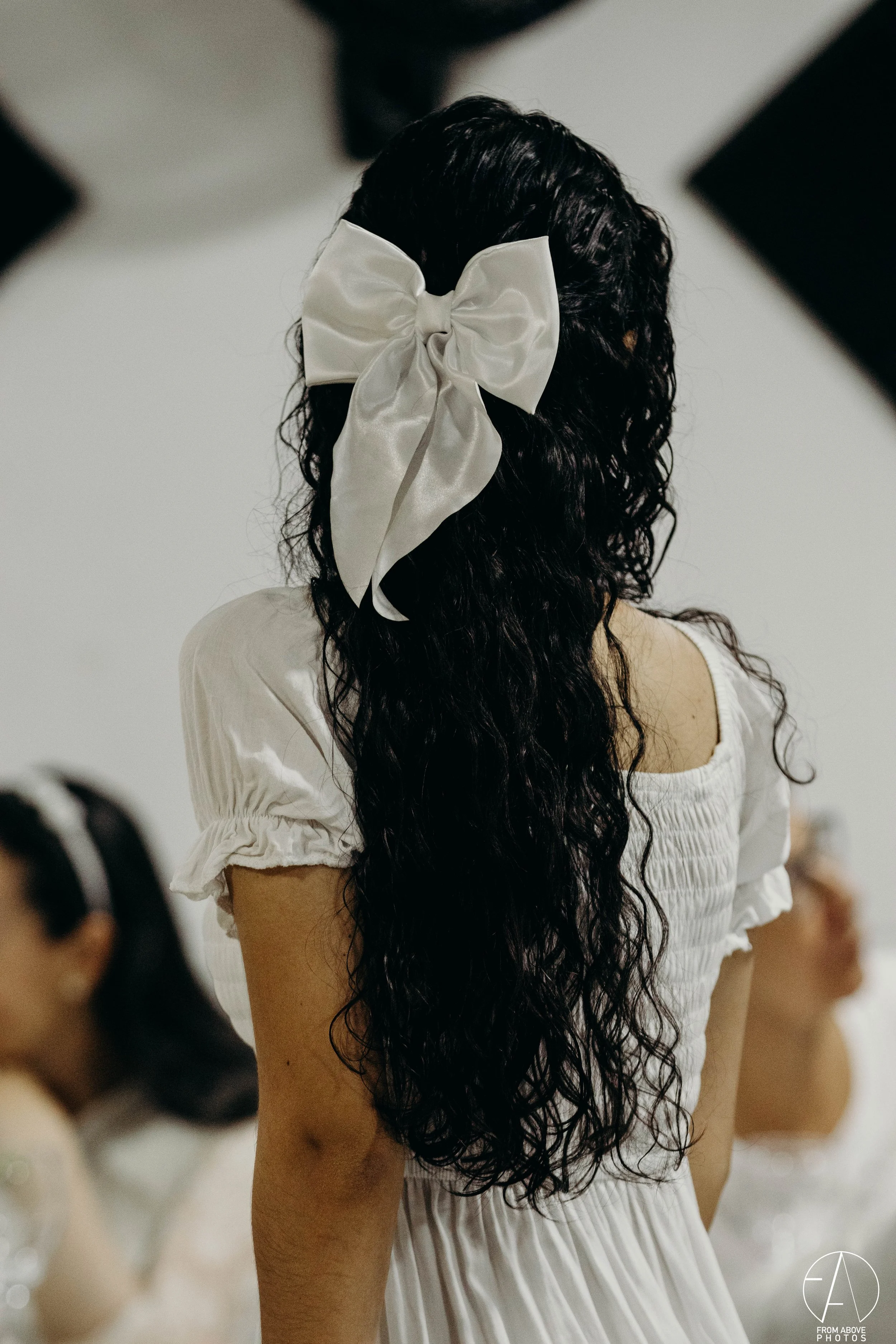 Mujer con cabello largo y rizado lleva un lazo blanco en la cabeza y un vestido blanco con mangas cortas y fruncidas.
