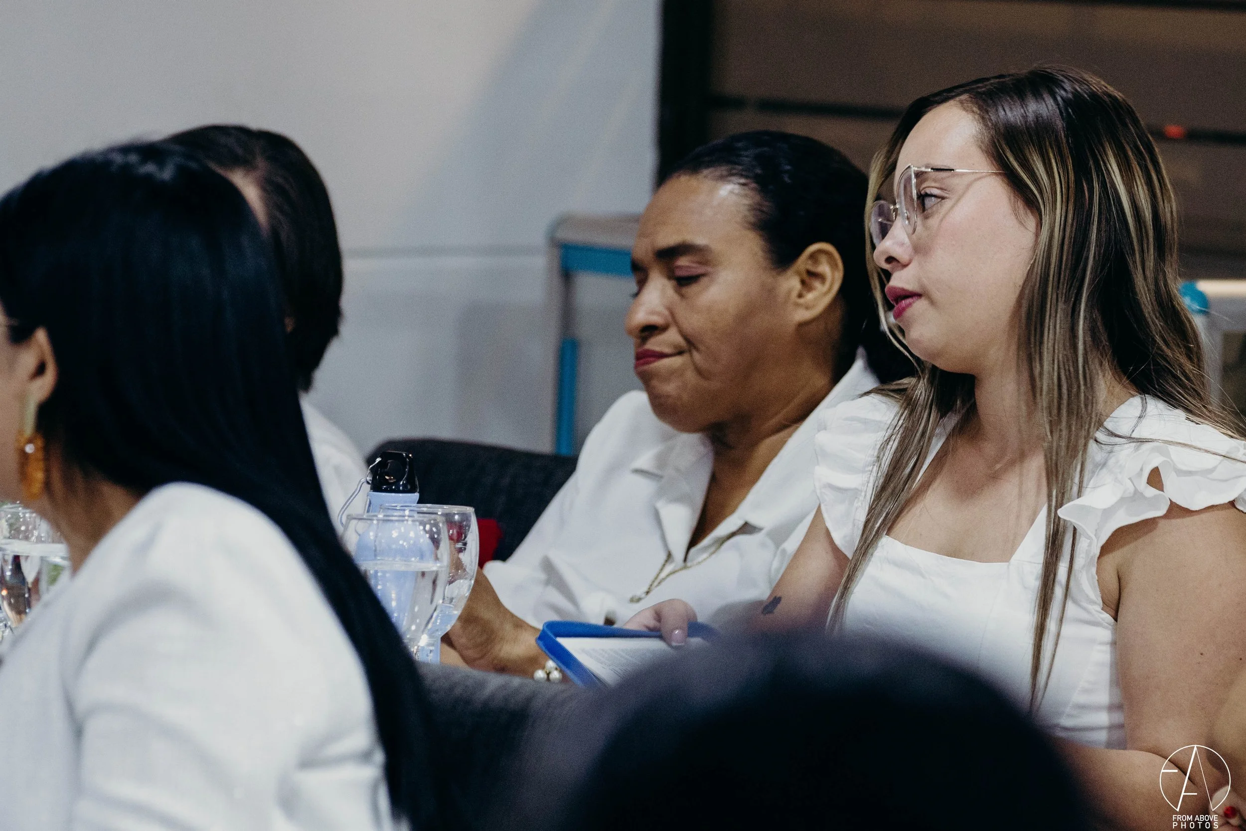 Seis mujeres sentadas en una mesa, algunas con ojos cerrados y otras mirando hacia abajo, en un ambiente de reunión o conferencia.