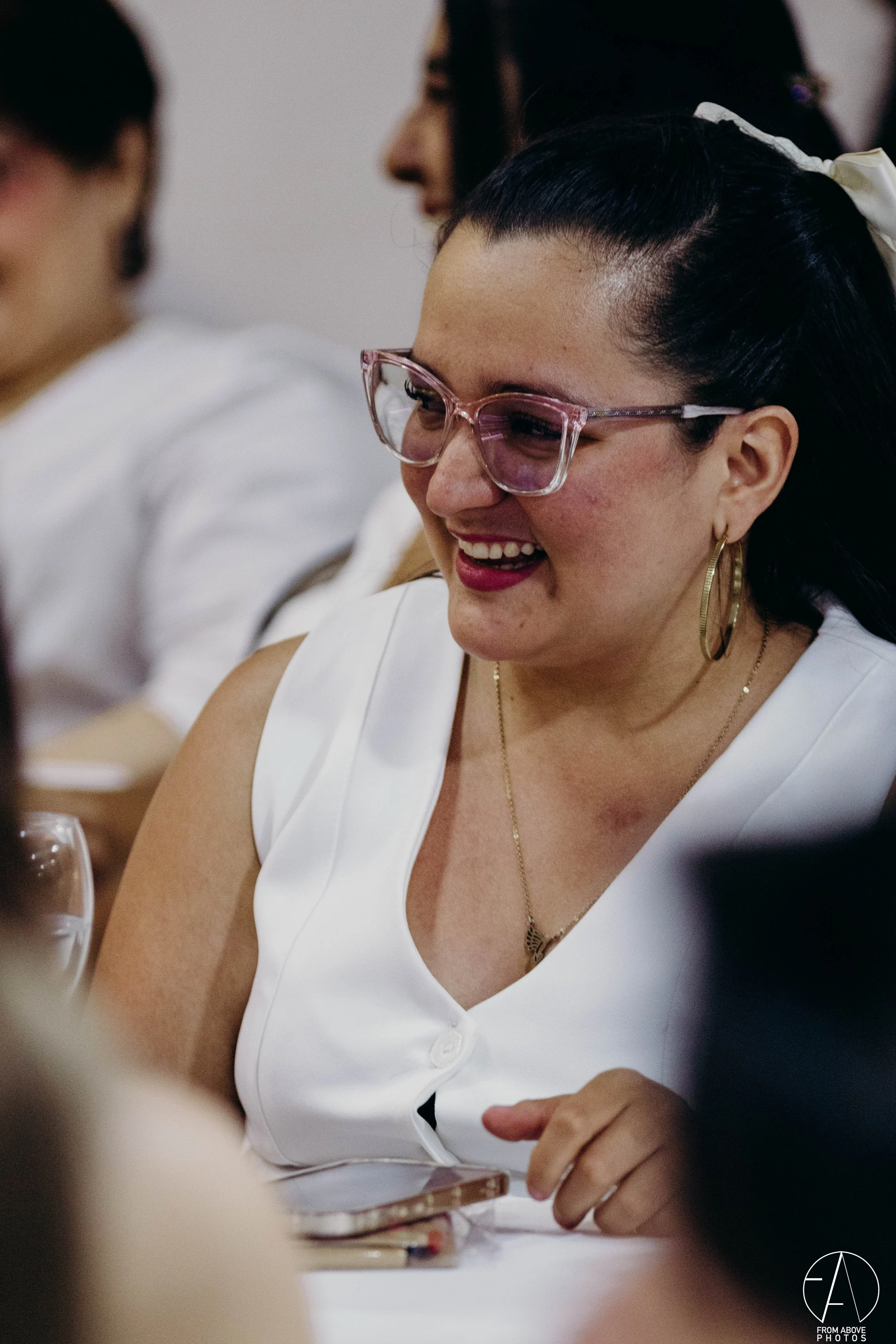 Mujer sonriendo con gafas rosas y pendientes dorados en una reunión o evento social