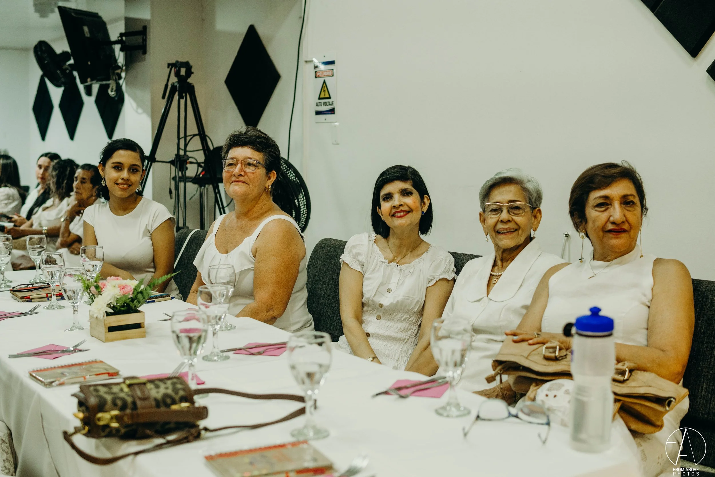 Grupo de mujeres sentadas en una mesa en un evento social, con decoraciones y utensilios en la mesa.