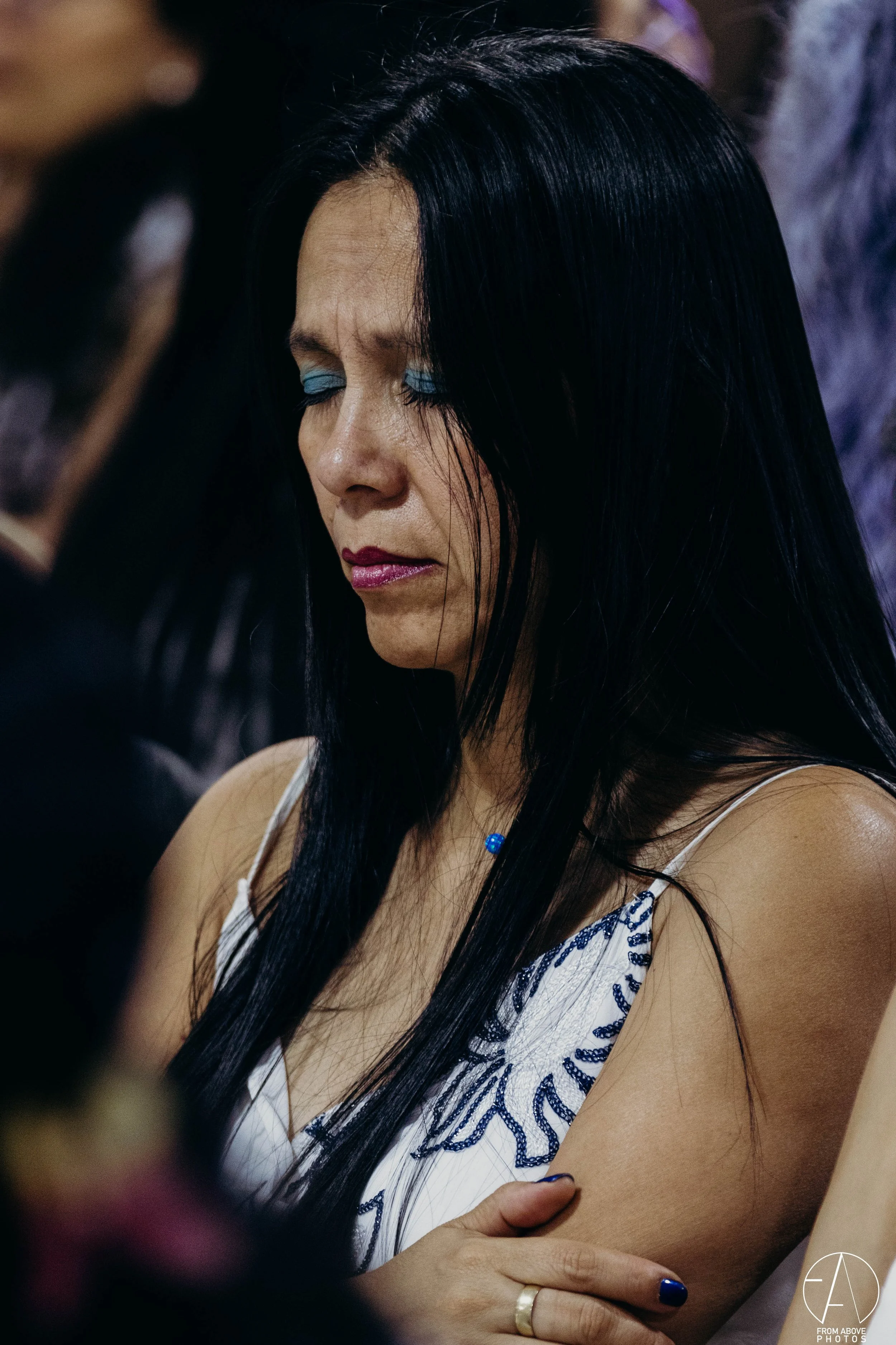 Mujer con cabello negro y maquillaje azul cerrando los ojos en un momento de introspección.
