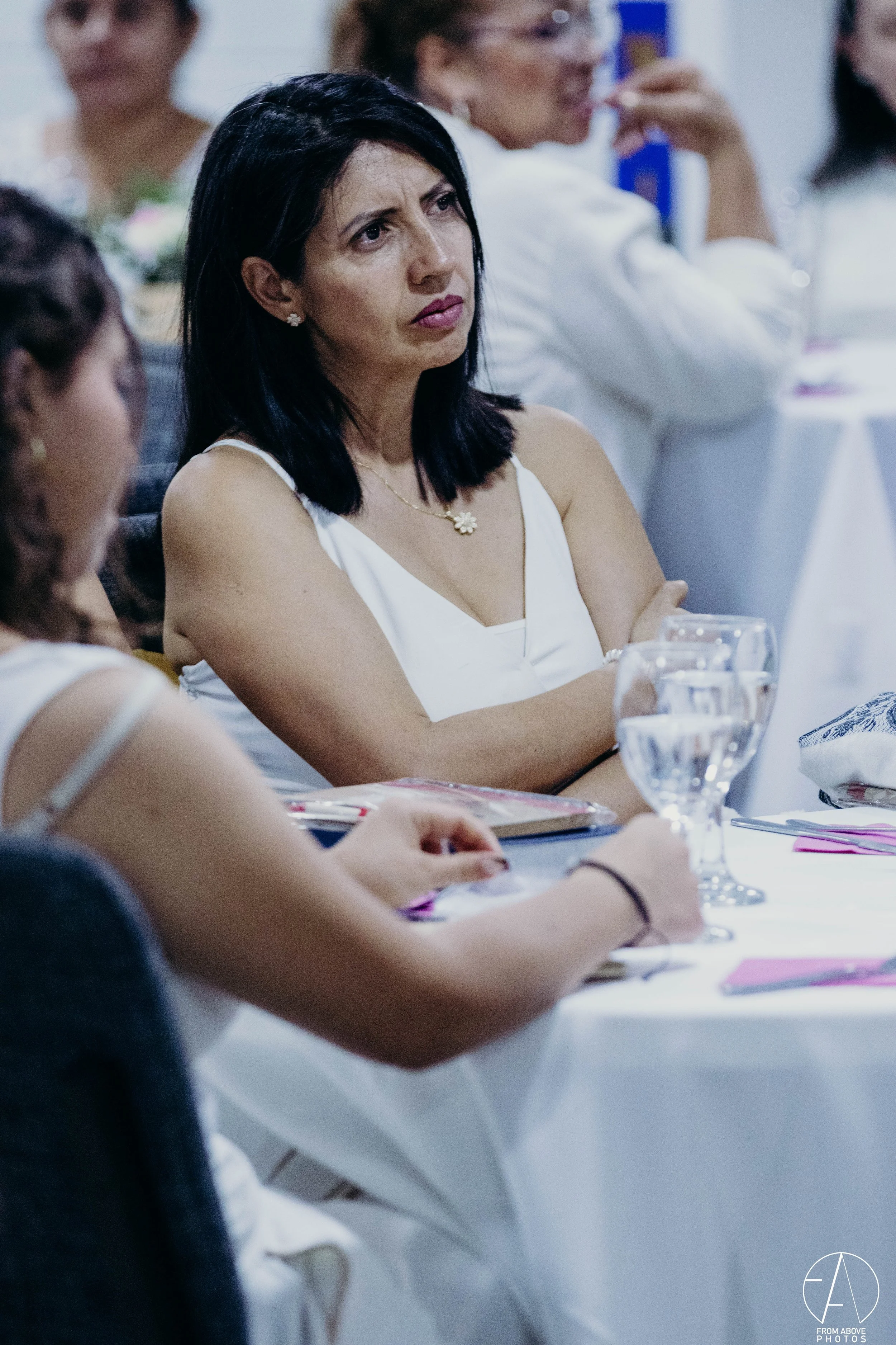 Mujer de cabello negro y ropa blanca escuchando atentamente en una reunión o conferencia.