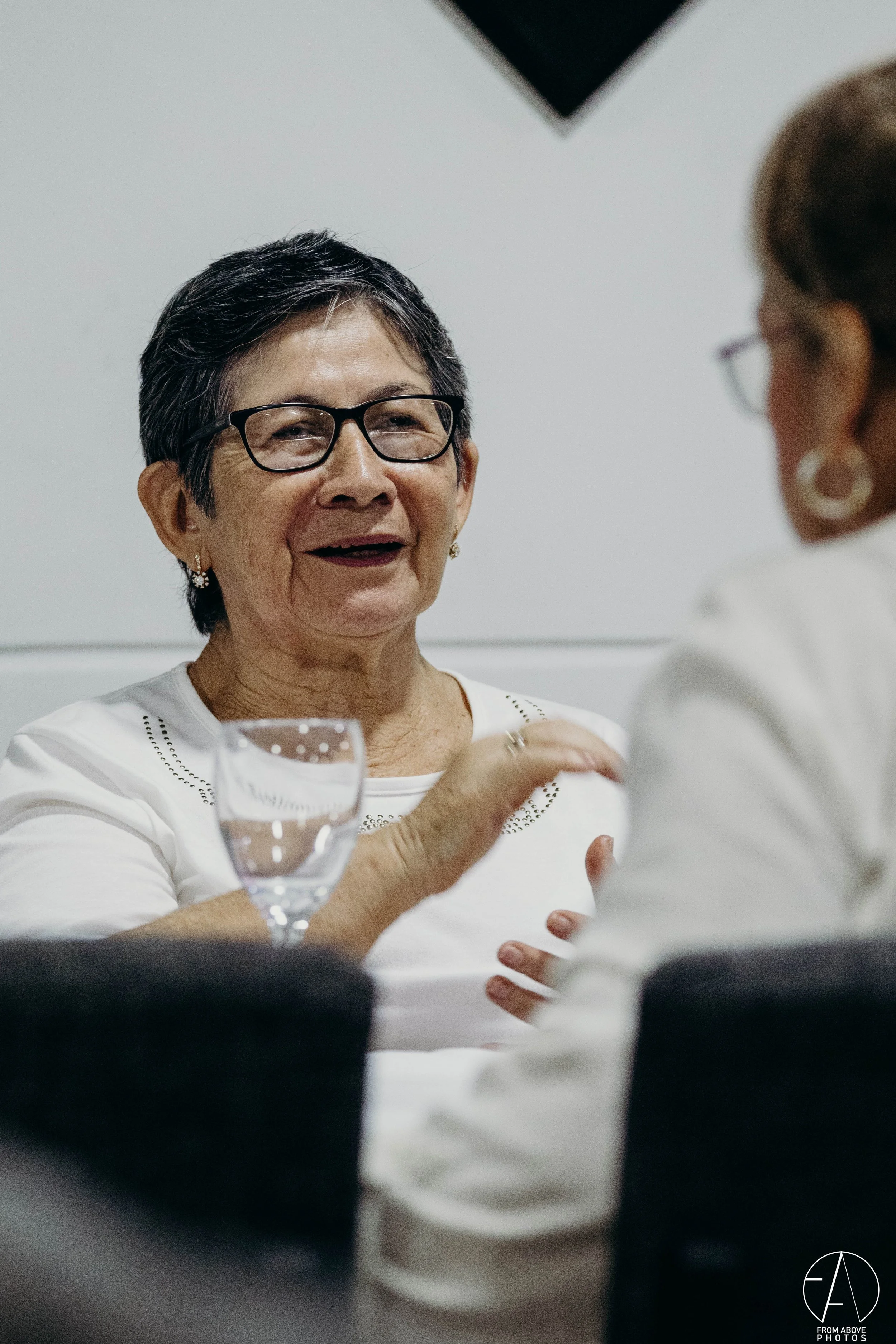 Mujer mayor hablando en una reunión, con una copa de agua en la mesa
