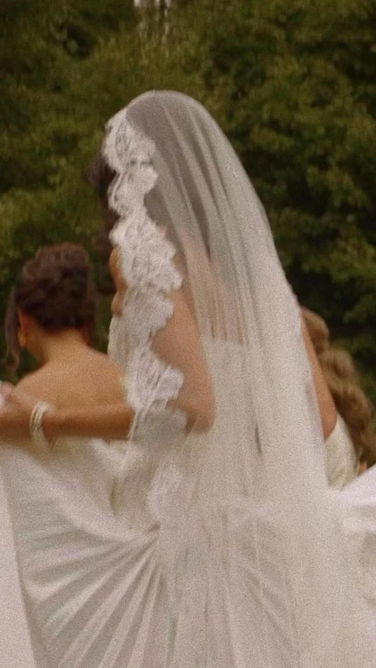 A bride in a white wedding gown with lace detailing and a veil dancing at her wedding reception with a woman in a sleeveless white dress.