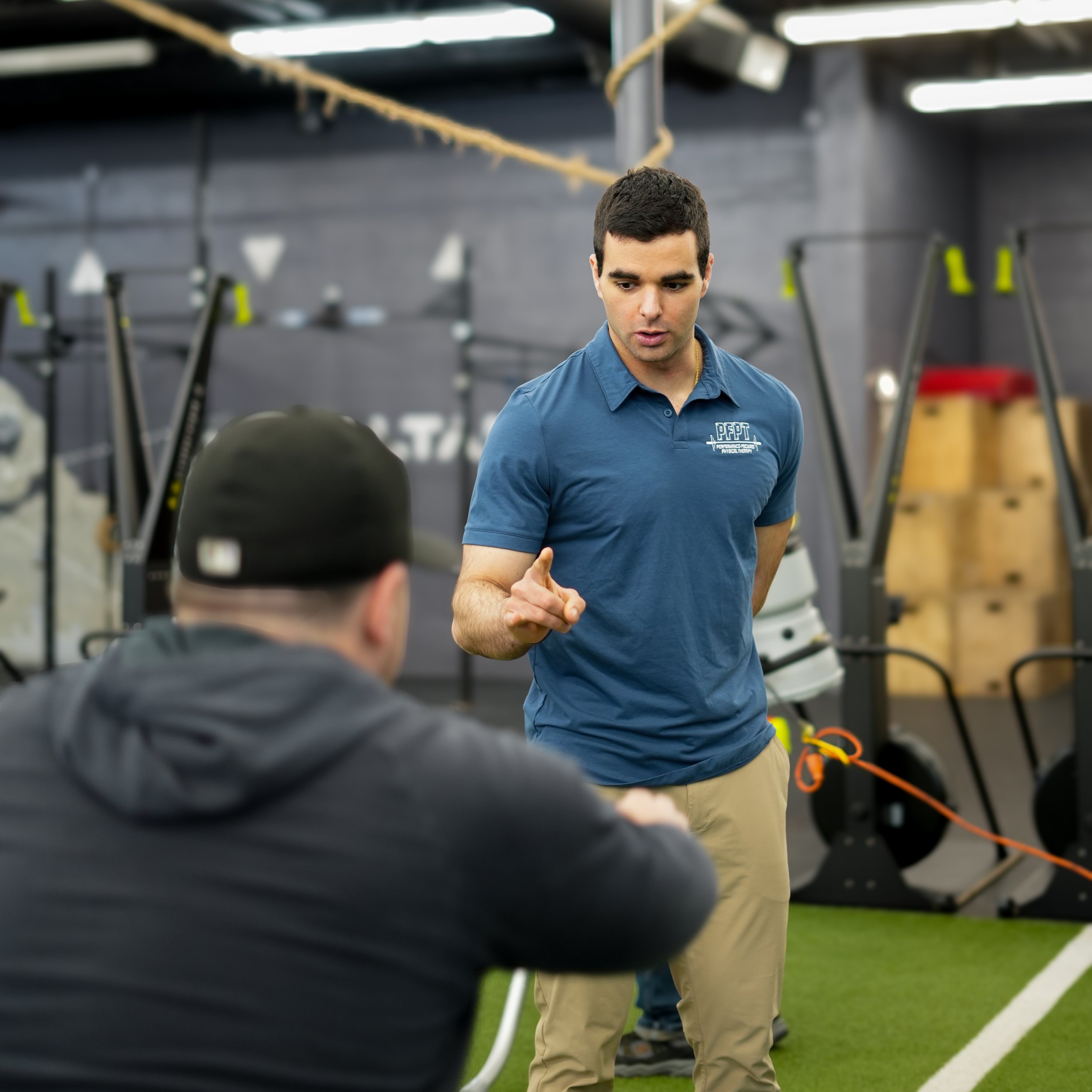 A man in a blue shirt teaching a class at a sports facility, with gym equipment in the background.