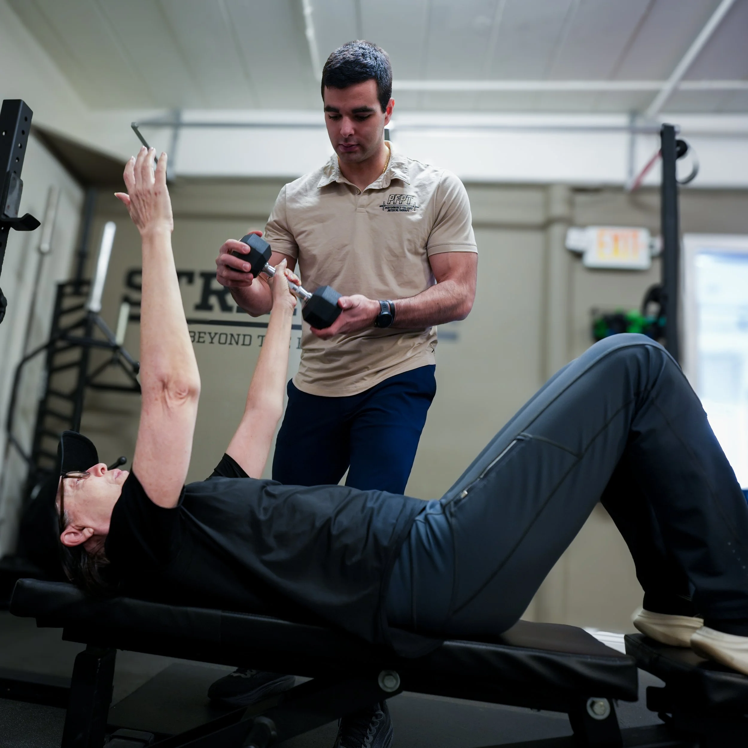 A fitness coach assisting a woman with exercises on a bench in a gym.