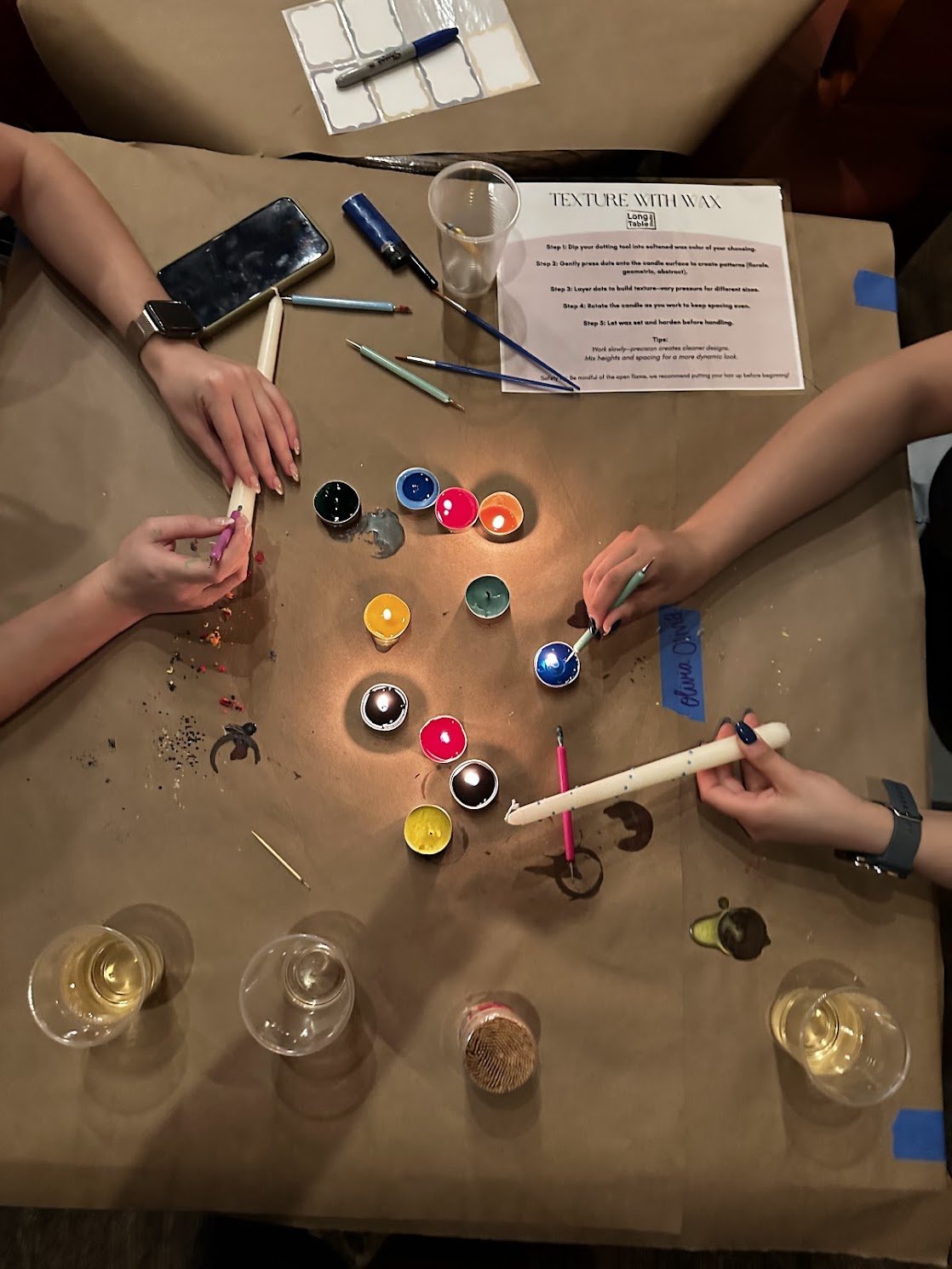 People painting candles with wax and candles, surrounded by open glasses of champagne.