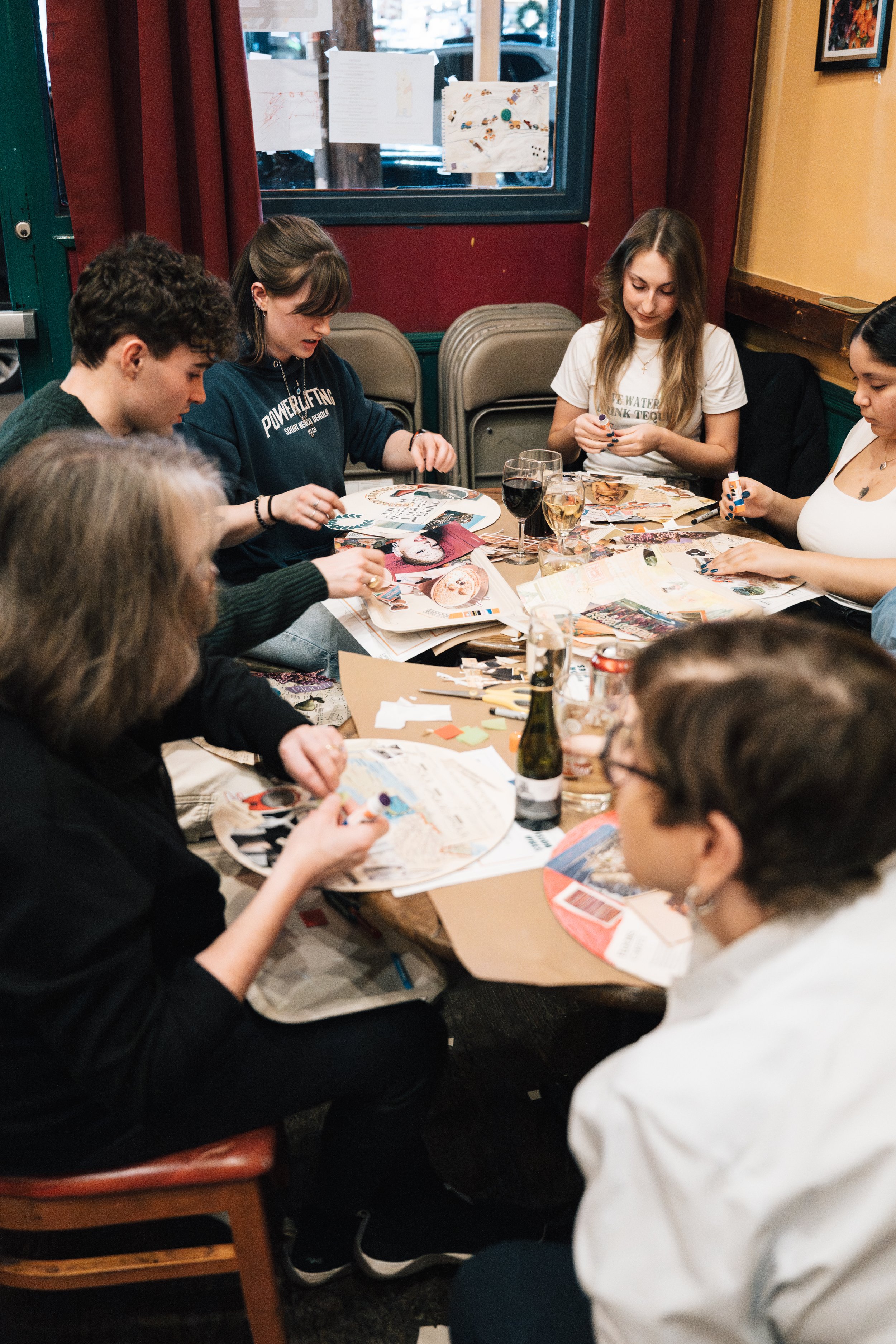 Group of young adults sitting around a table, engaging in arts and crafts activities at a restaurant or cafe.
