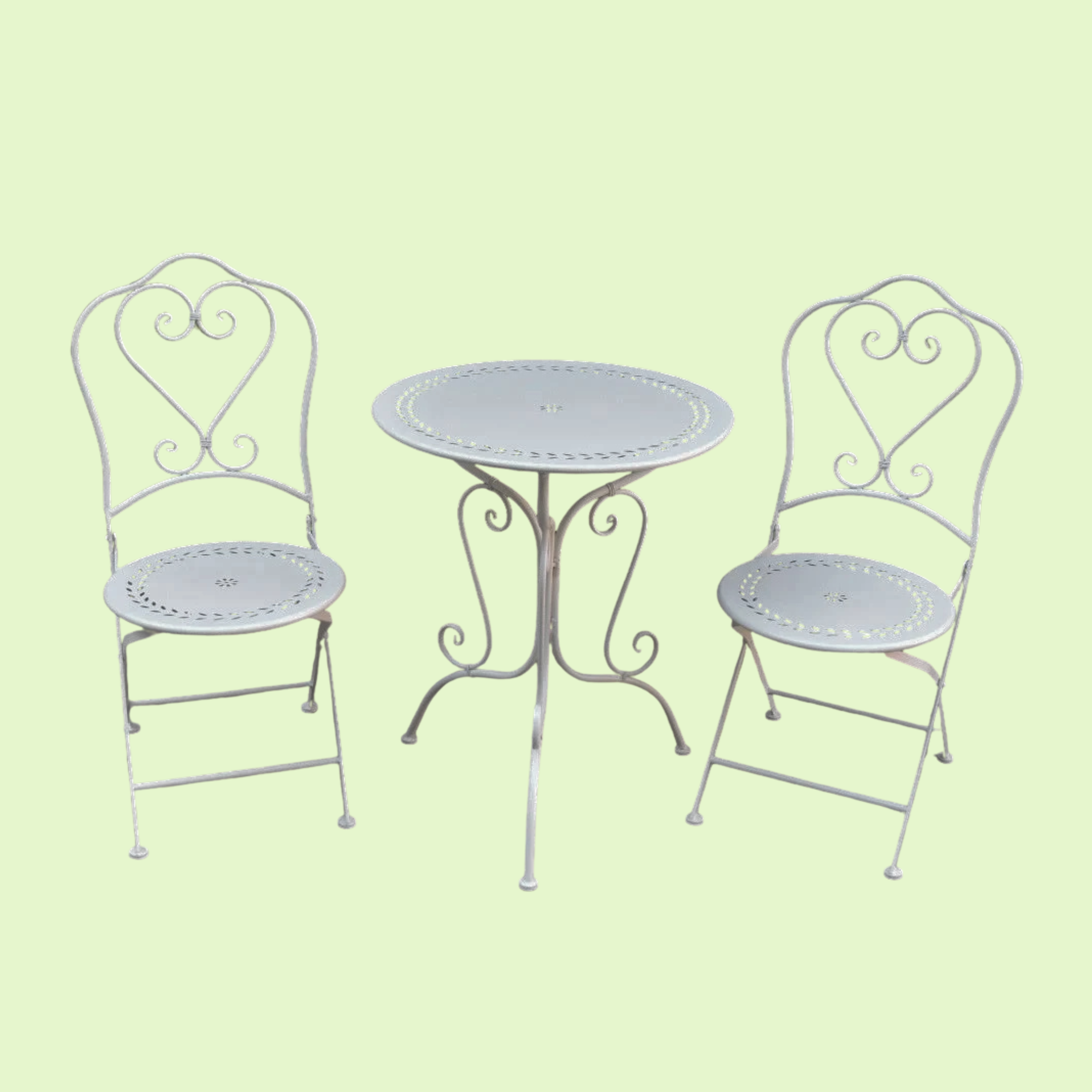 White wrought iron patio table with two matching chairs on a light green background.