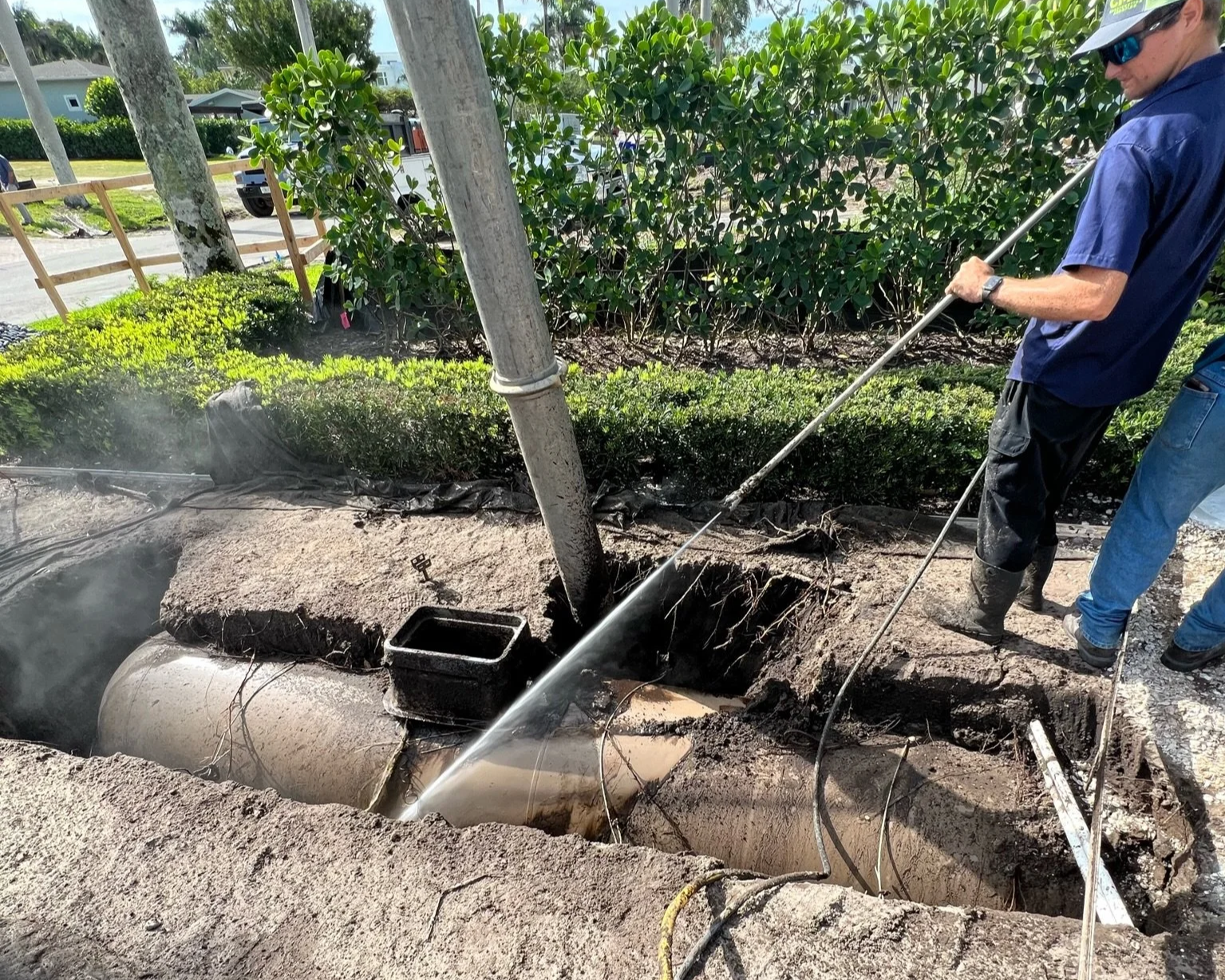 Hydro excavation crew using high-pressure water to expose a buried drainage pipe during a utility locate in Naples, Florida.