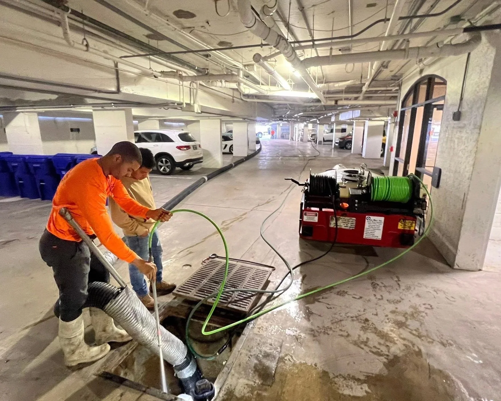 Technician performing stormwater system maintenance and catch basin cleaning inside a parking garage in Southwest Florida.
