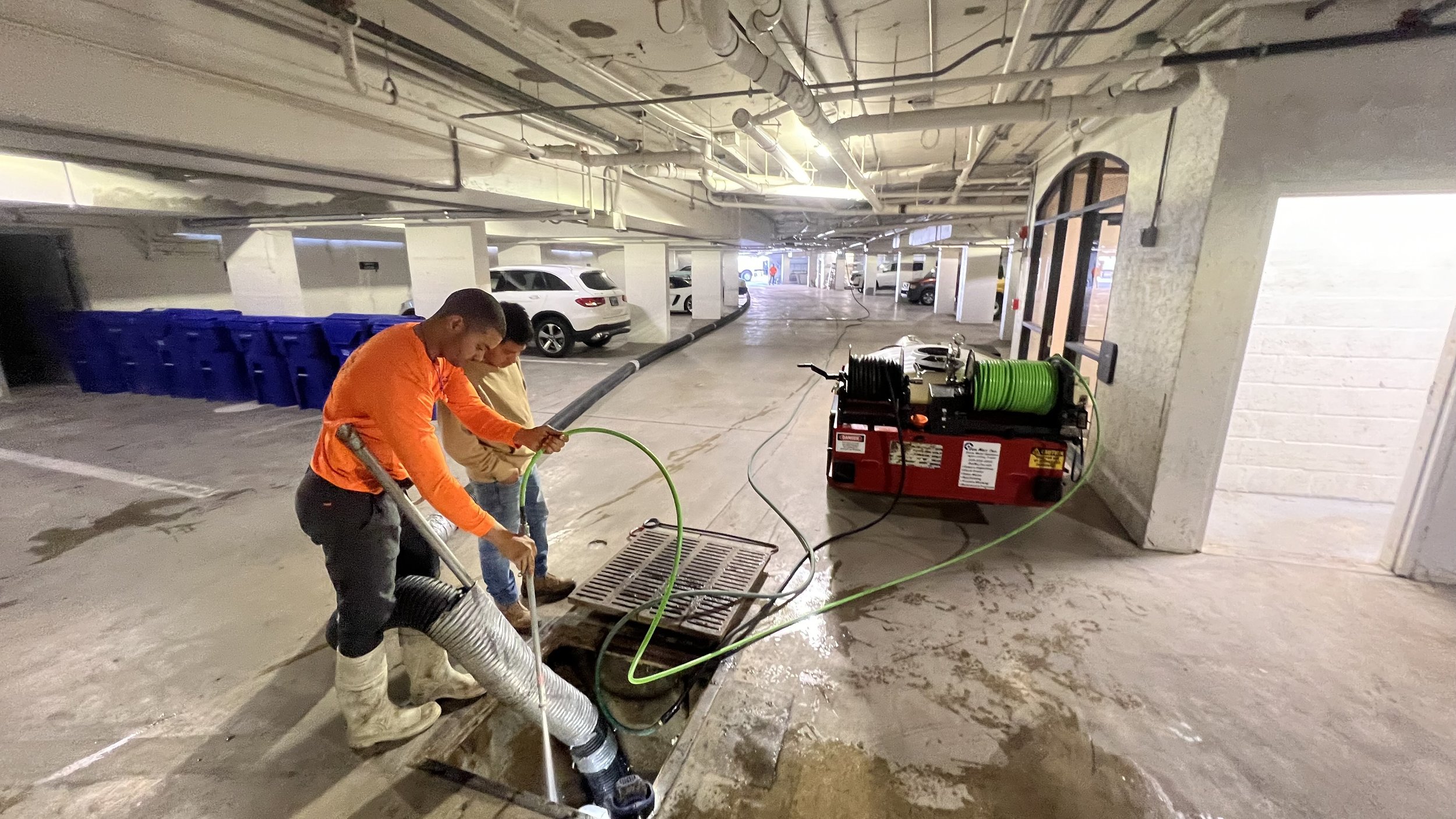 Stormwater maintenance crew jetting and cleaning a catch basin inside a parking garage in Southwest Florida.