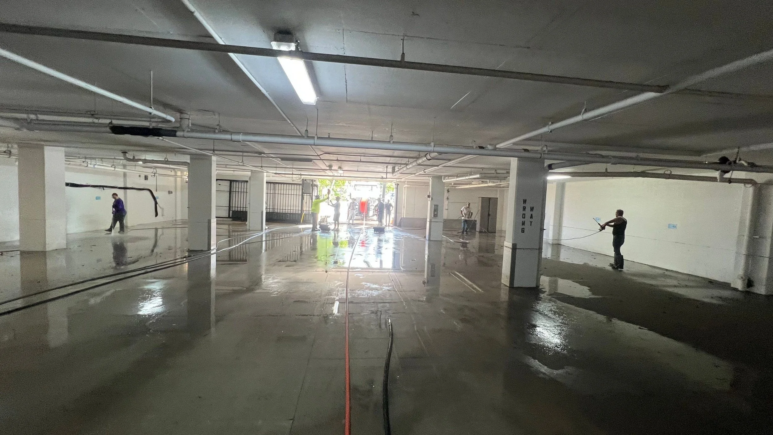 Technicians performing high-flow commercial surface cleaning inside a parking garage in Southwest Florida.