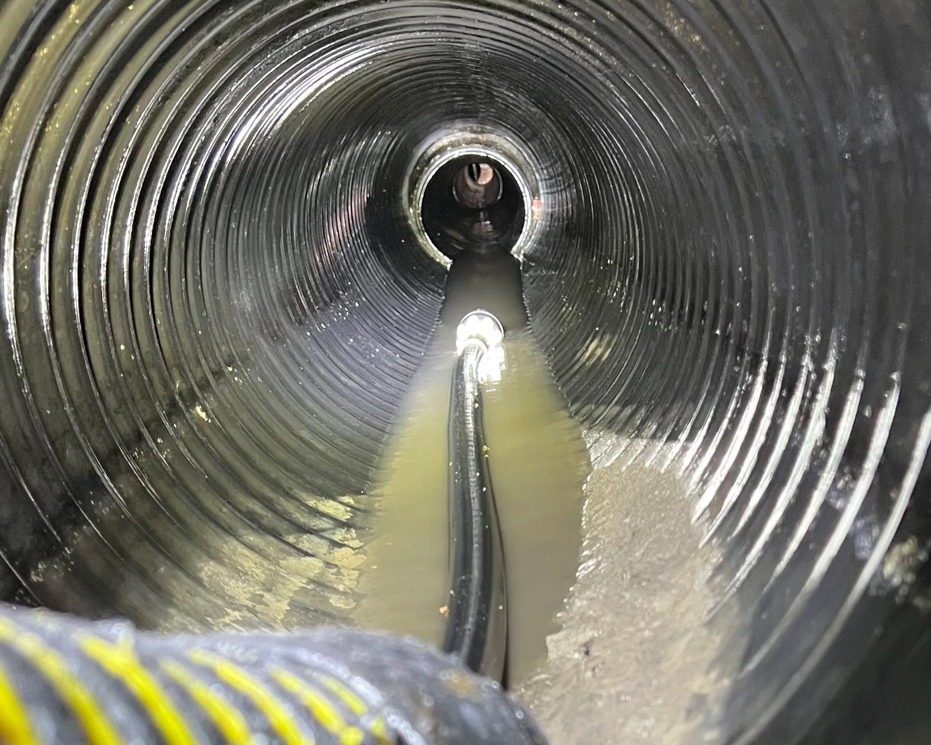 High pressure hydro jetting nozzle cleaning inside a corrugated drainage pipe to remove blockages.