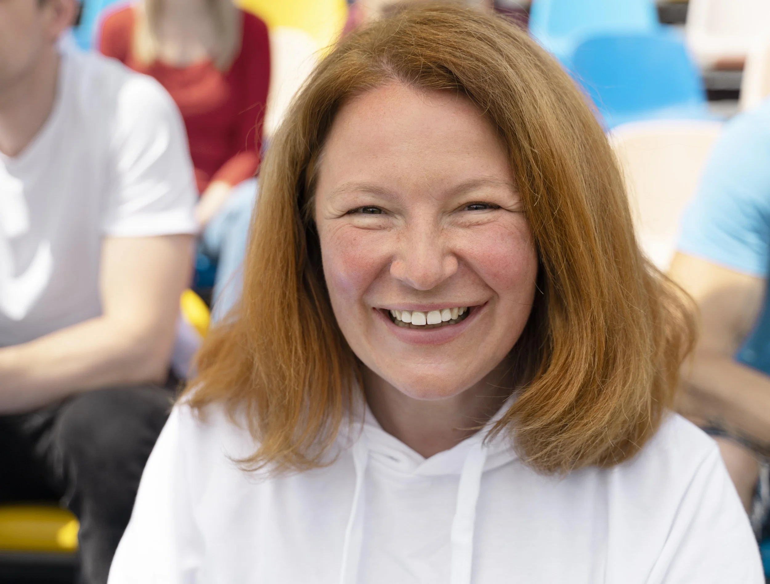 A smiling woman with shoulder-length black hair, wearing a blue top, standing among green foliage.