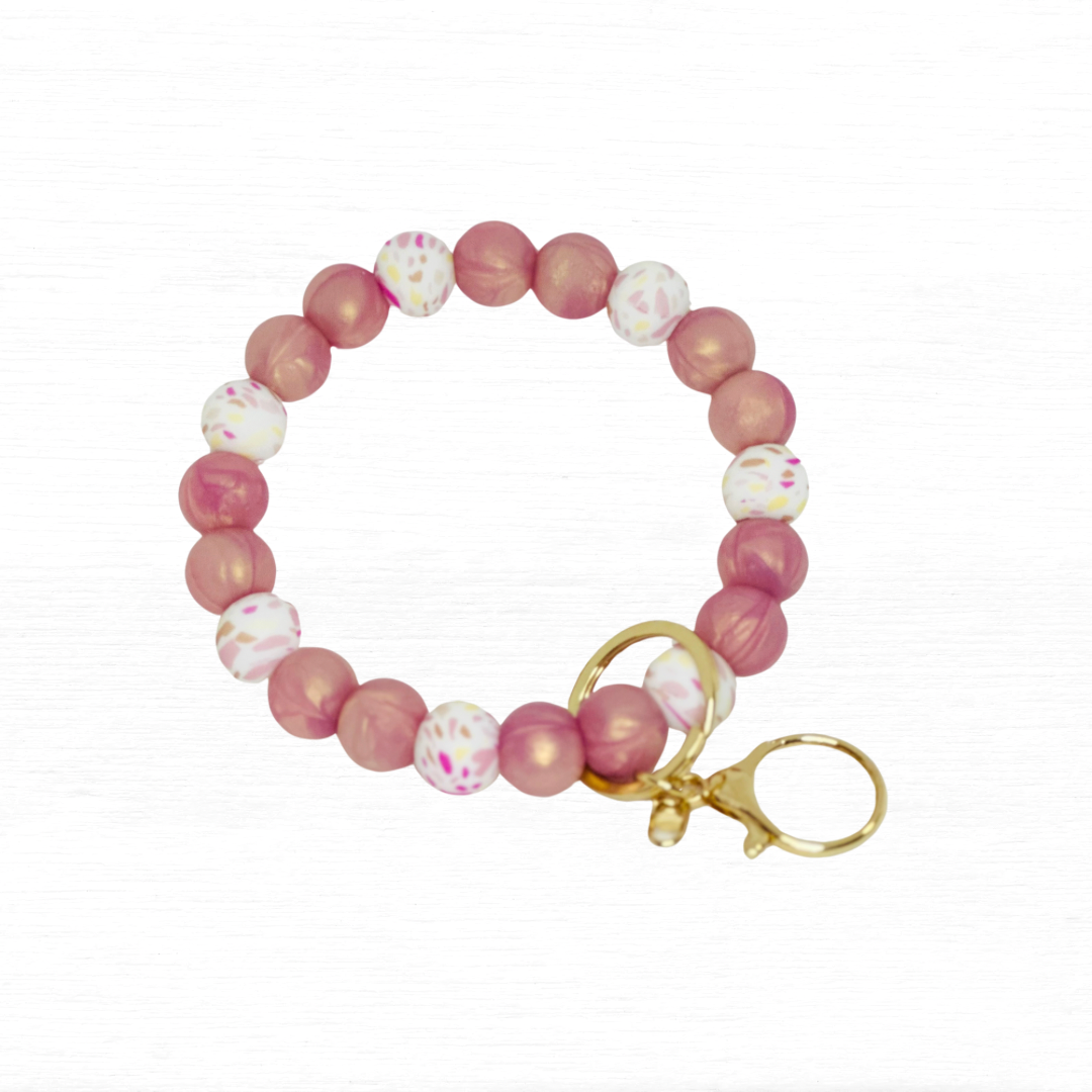 Pink and white beaded bracelet with gold clasp on a light background.