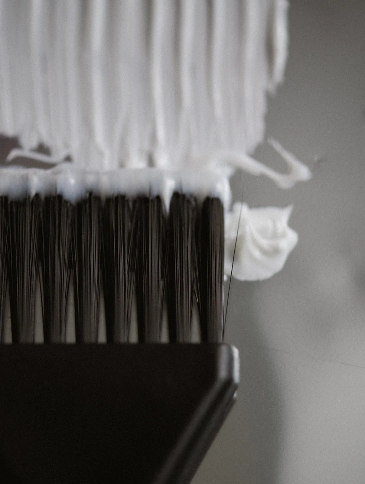 Close-up of a hairbrush with black bristles and white hair product or foam on it.