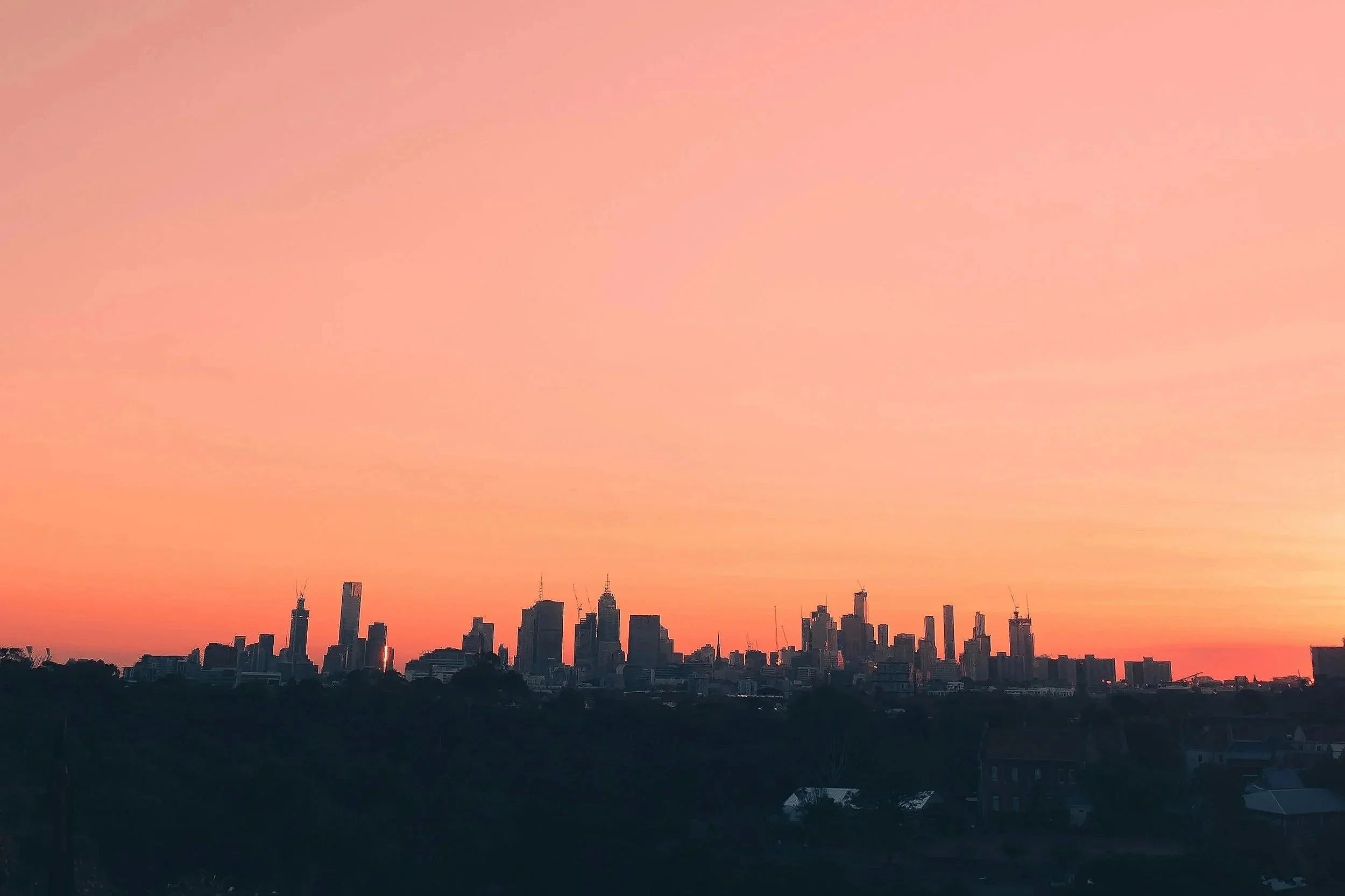 Skyline of a city at sunset with tall buildings and a pink-orange sky.