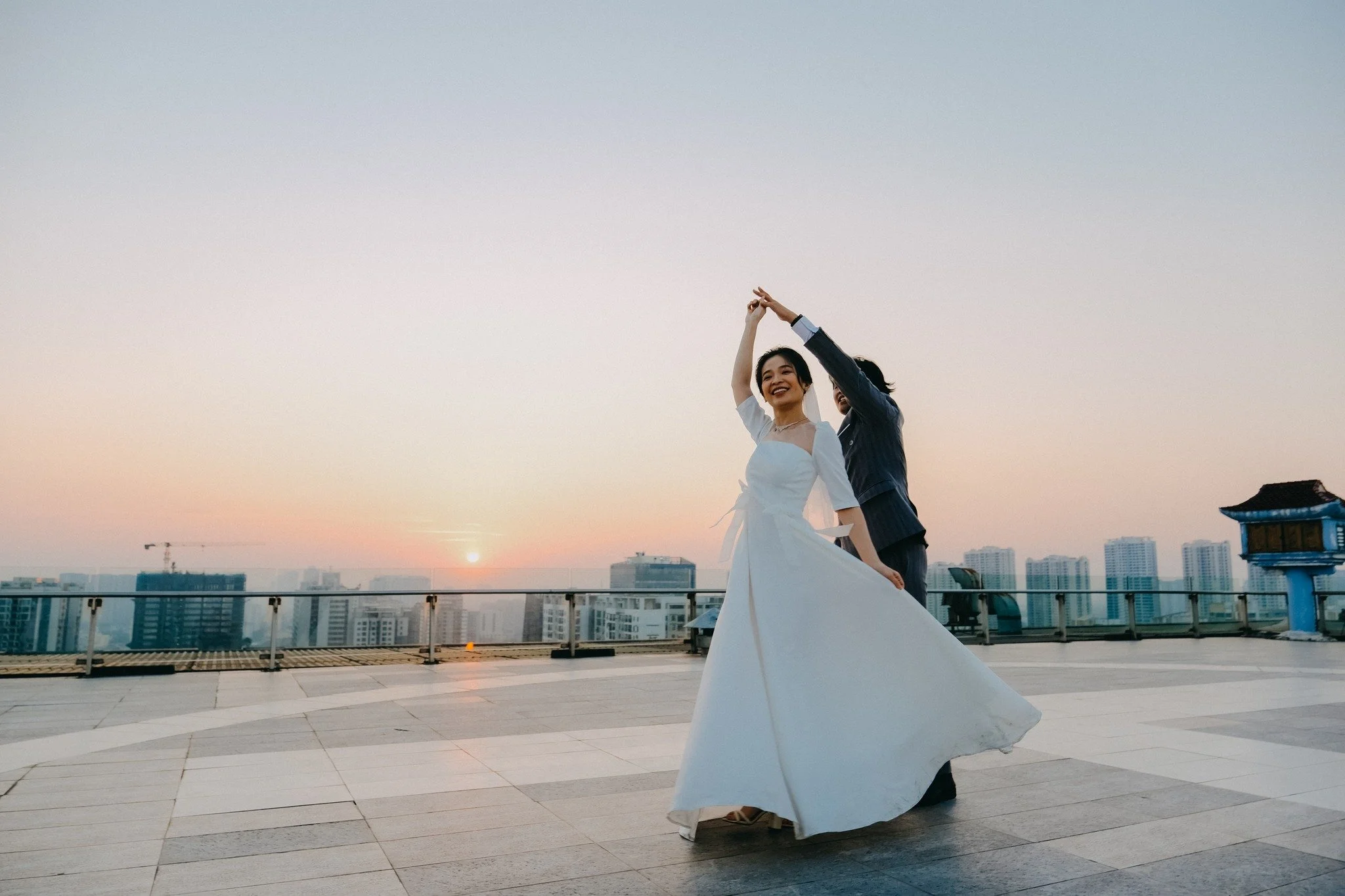 Two women dancing on a rooftop during sunset in a city.