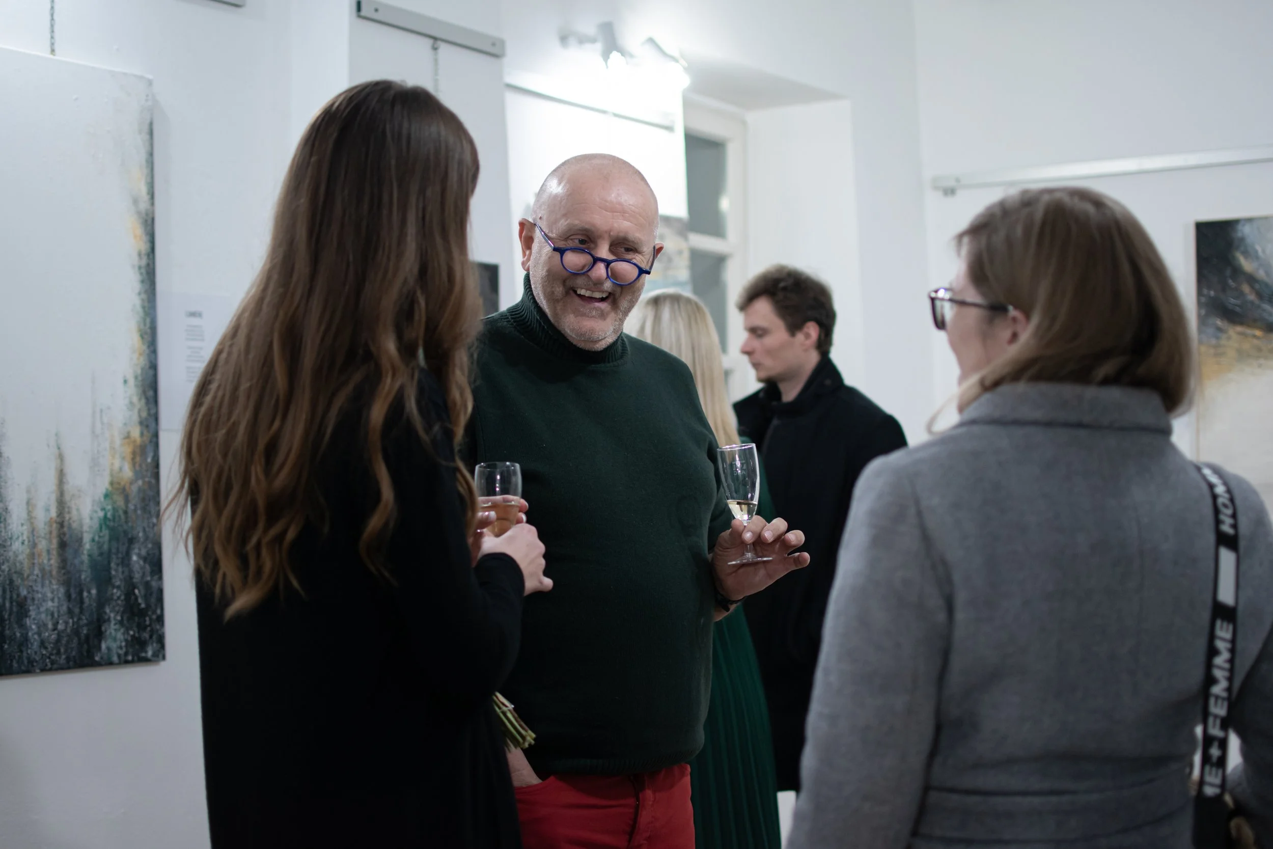 People talking at an art gallery, holding glasses of champagne.