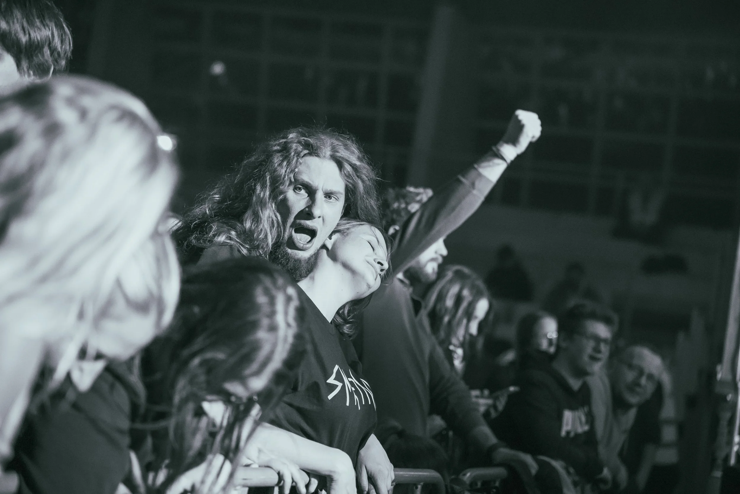 Group of people at a concert or event, with some raising their fists or looking excited, black and white photograph.