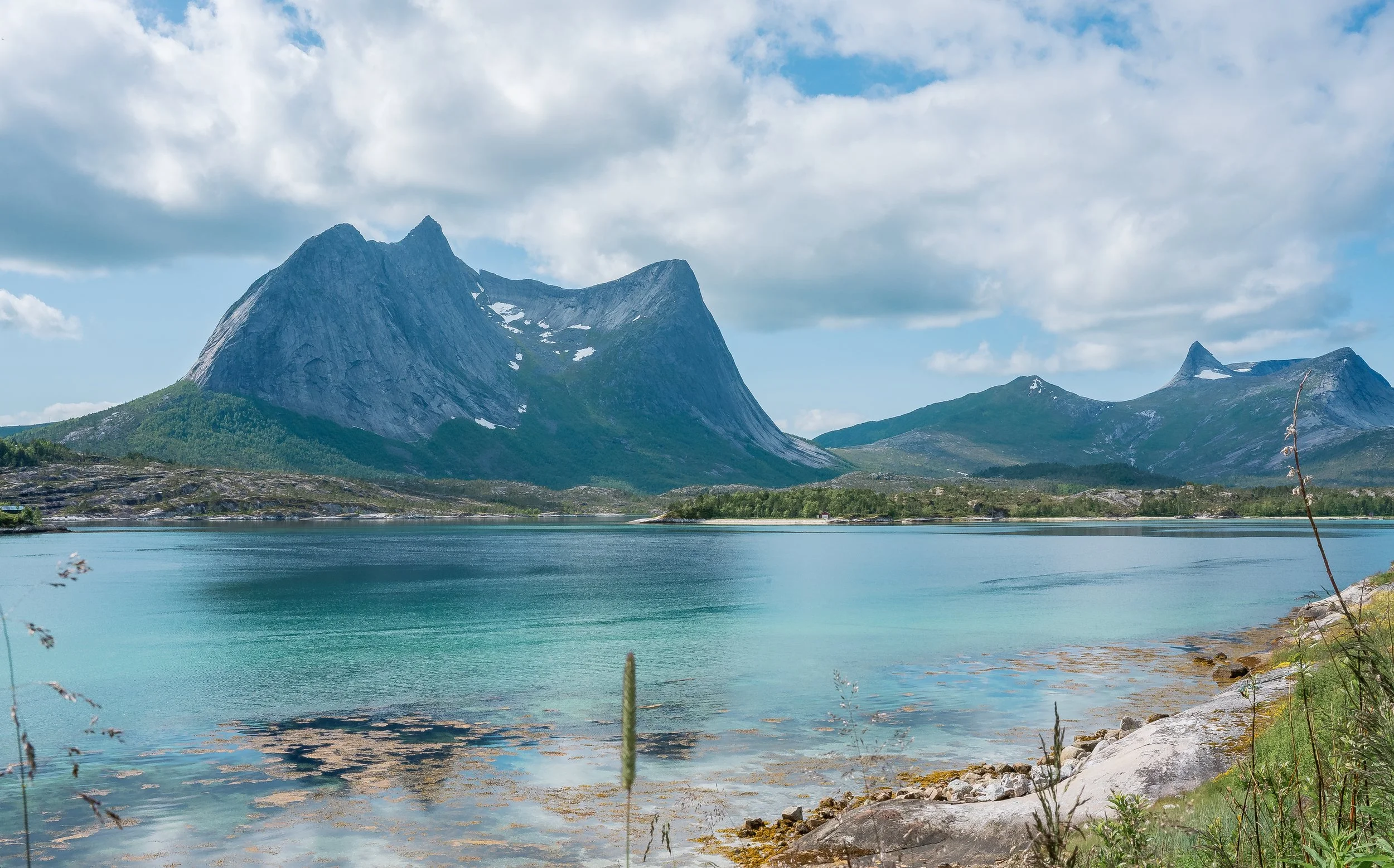 Scenic landscape with a mountain range, a calm lake, and partly cloudy sky.
