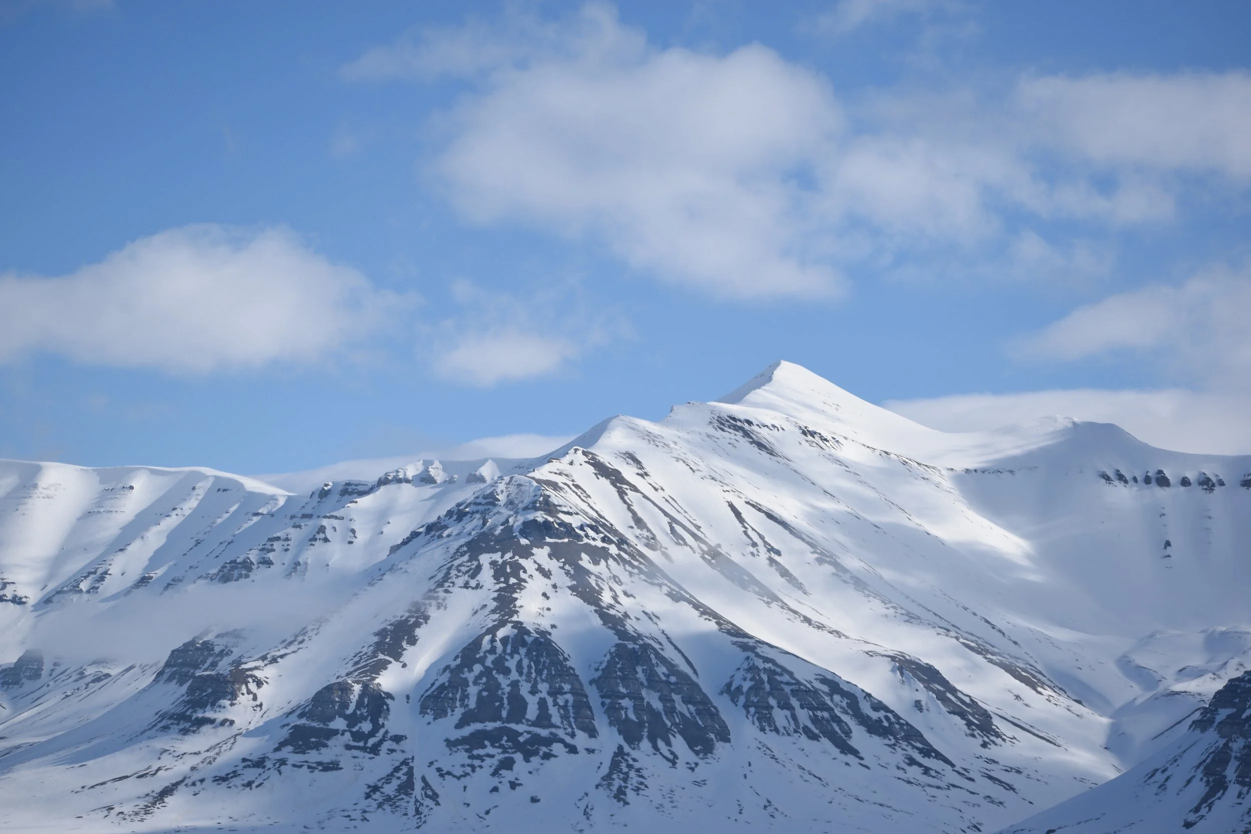 Snow-covered mountain peaks under a partly cloudy blue sky.
