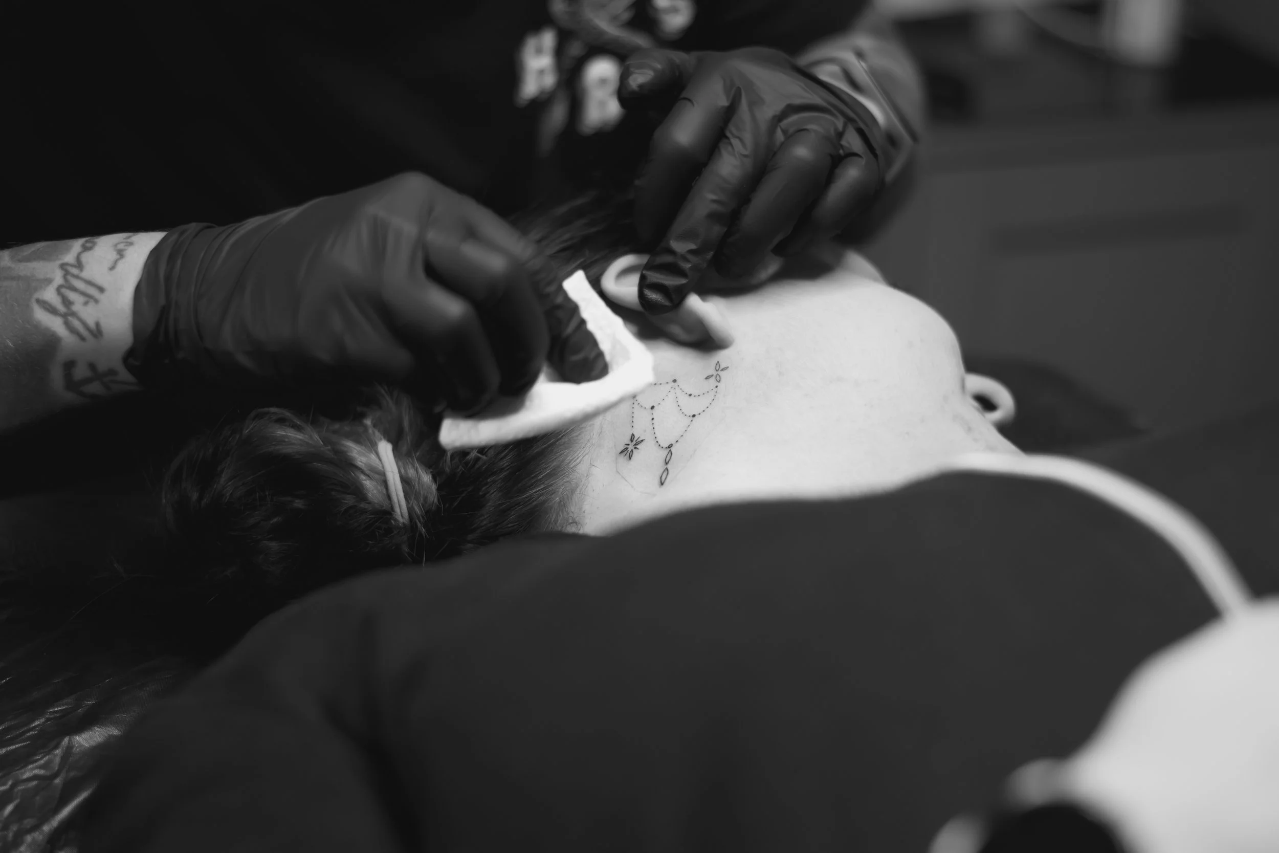 A person getting a tattoo on their neck while lying down.