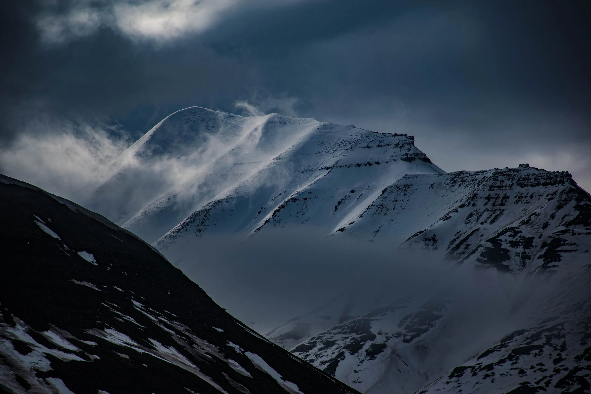 Snow-covered mountain peaks under dark cloudy sky.